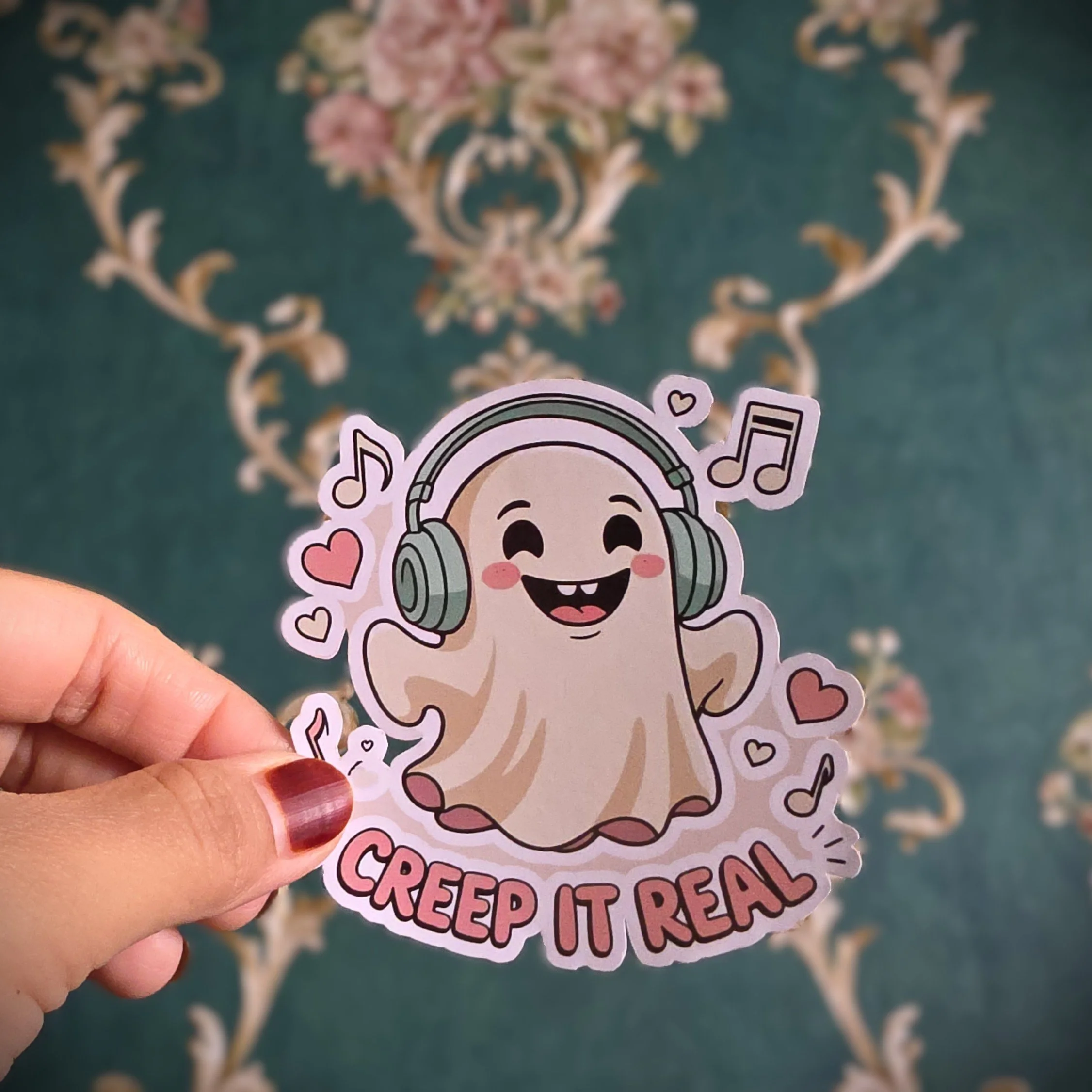 A sticker featuring a cute cartoon ghost with a big smile, pink cheeks, and wearing large headphones. The ghost is surrounded by musical notes and hearts, and the words 'Creep It Real' are written at the bottom.