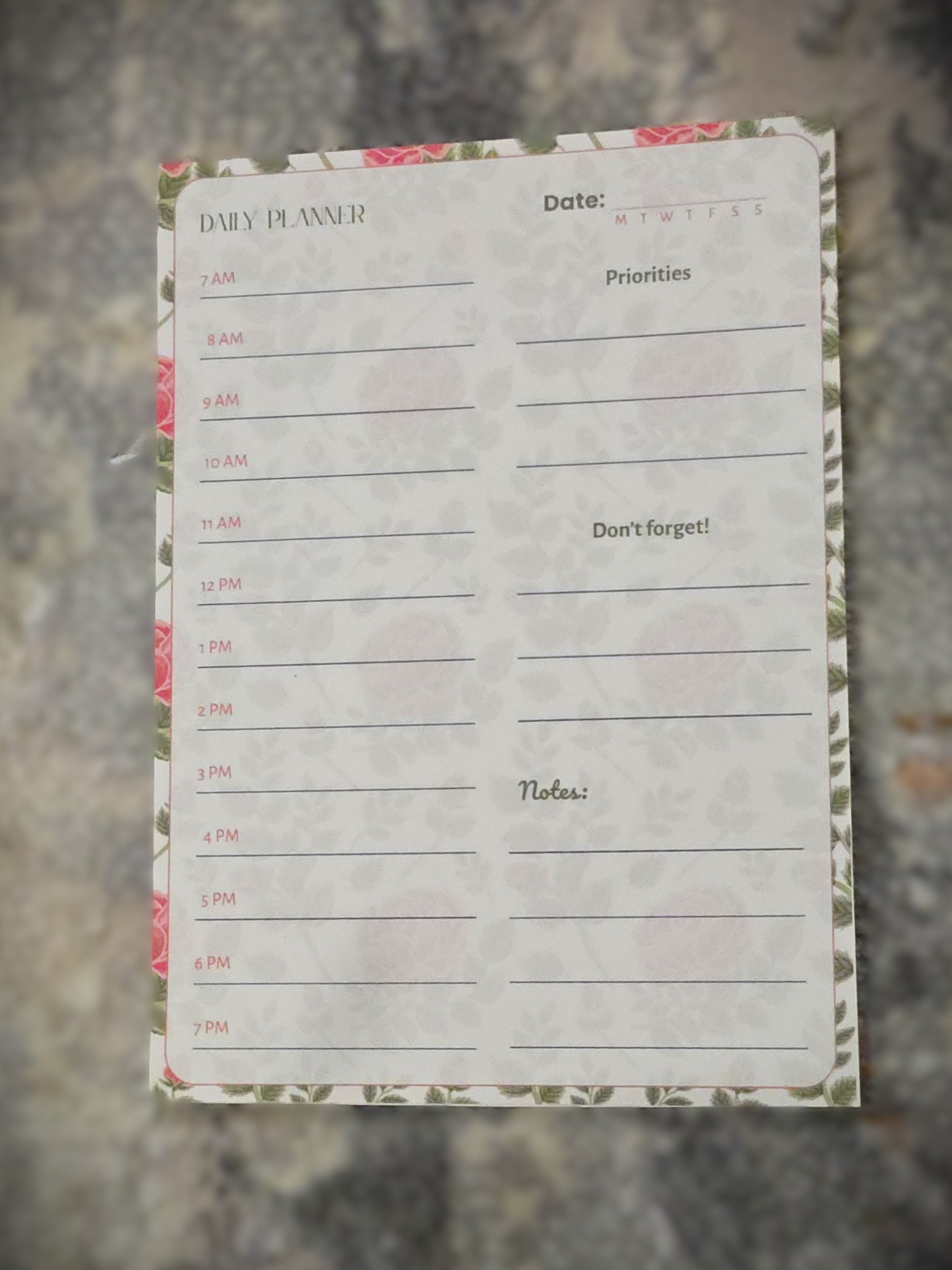 A floral patterned daily planner with time slots from 7 a.m. to 7 p.m., space for priorities, a reminder not to forget, and notes, displaying a blank schedule.