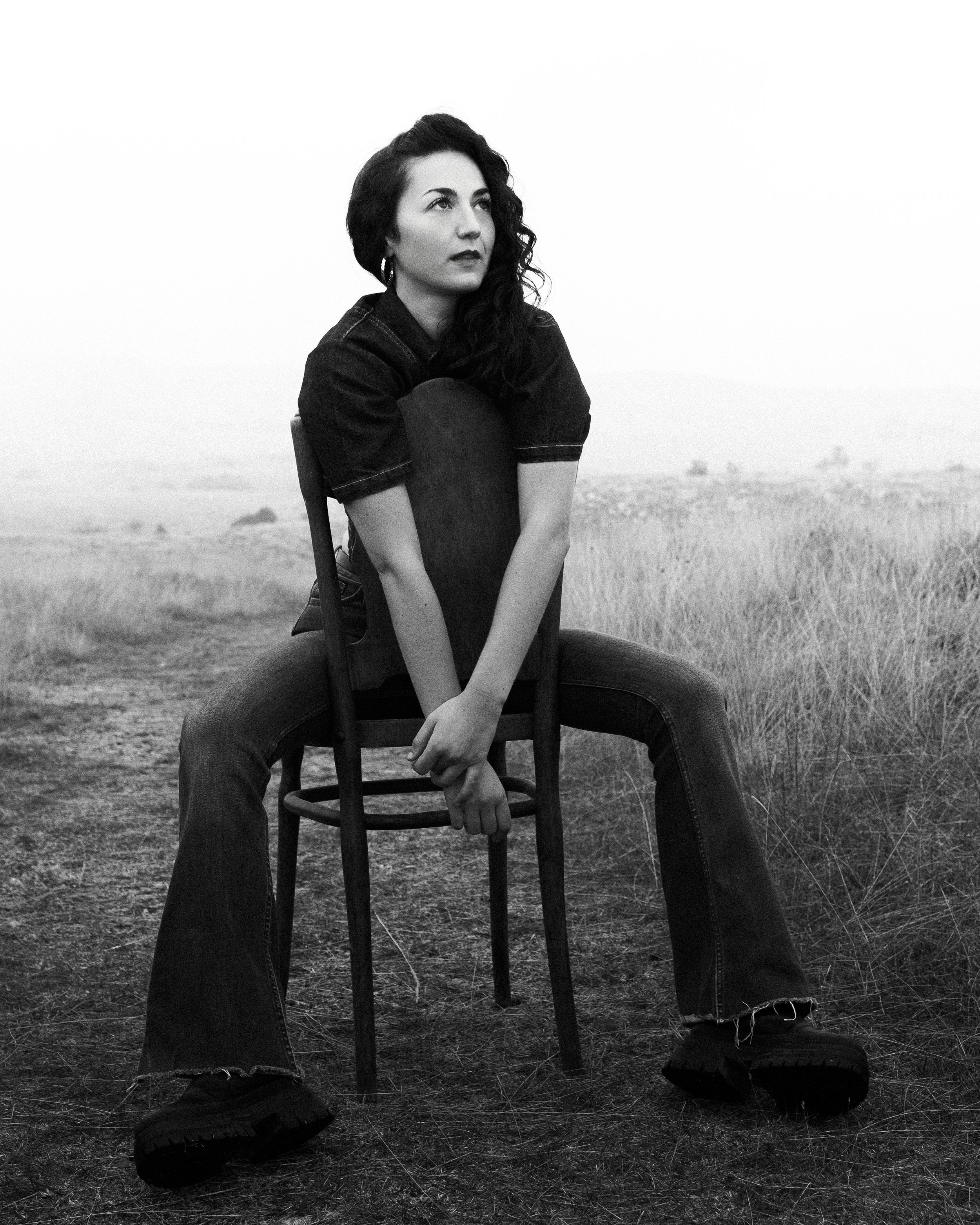 Une femme assise sur une chaise dans un champ, regardant vers la gauche, en noir et blanc.