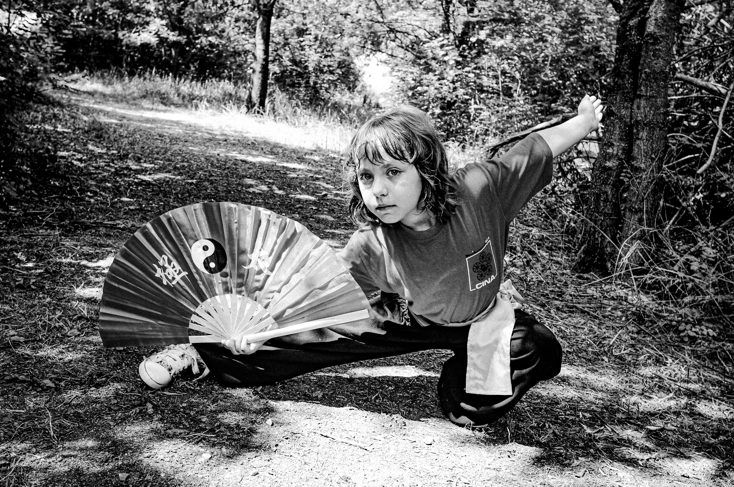 Bambino in posa in un bosco con un ventaglio decorato con simboli taoisti e il logo di Cina, vestito con abbigliamento sportivo.