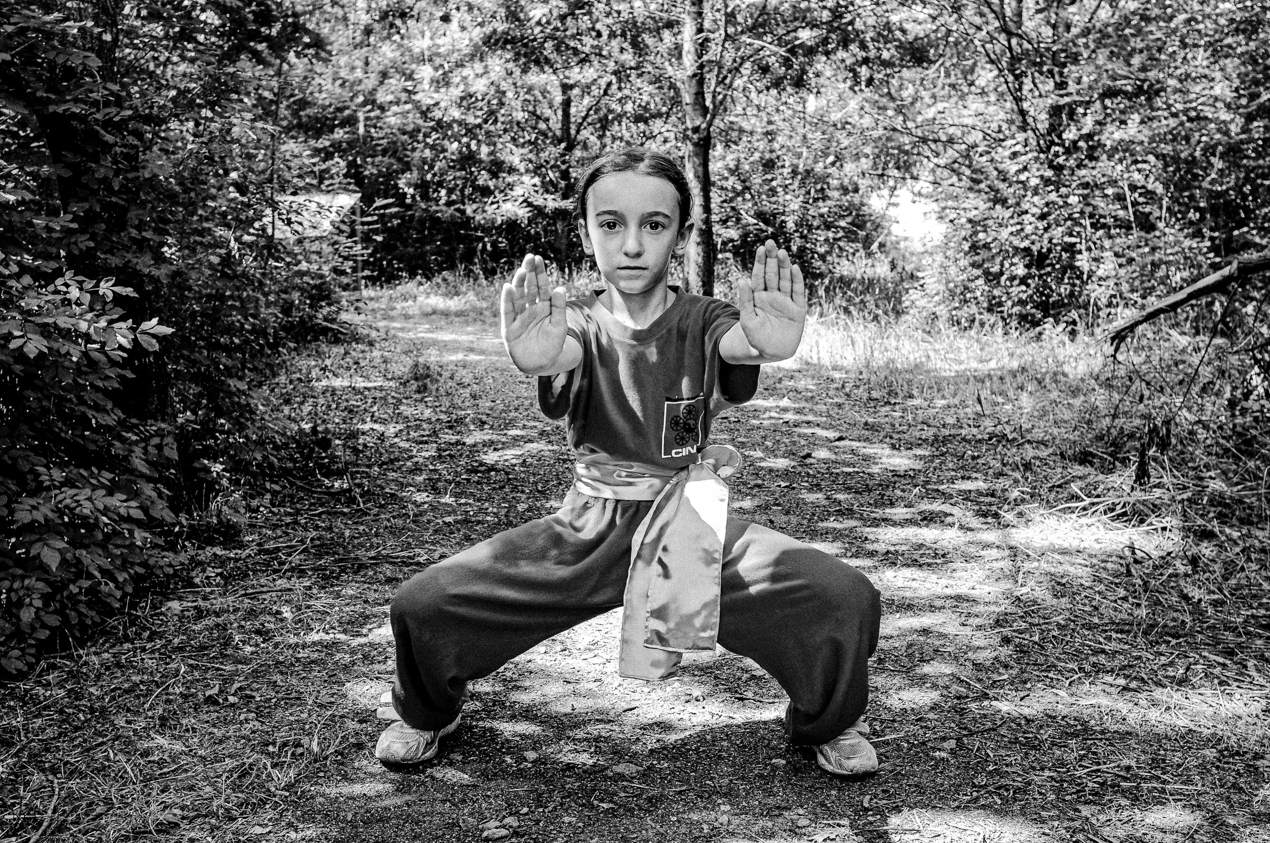 Bambina in posa di difesa con gambe divaricate e mani davanti, in una foresta