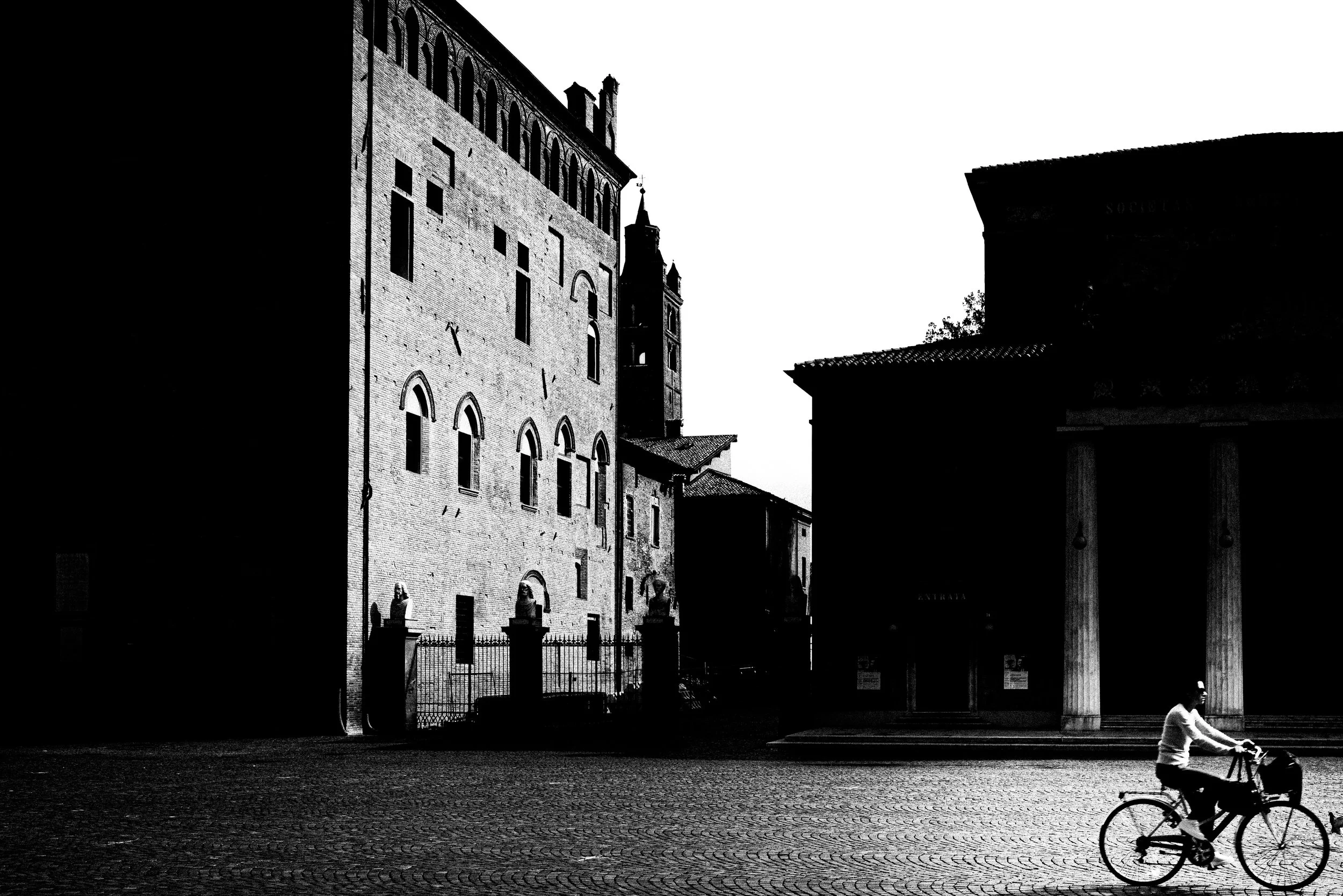 Scena urbana in bianco e nero con edificio storico e un ciclista che passa di fronte.