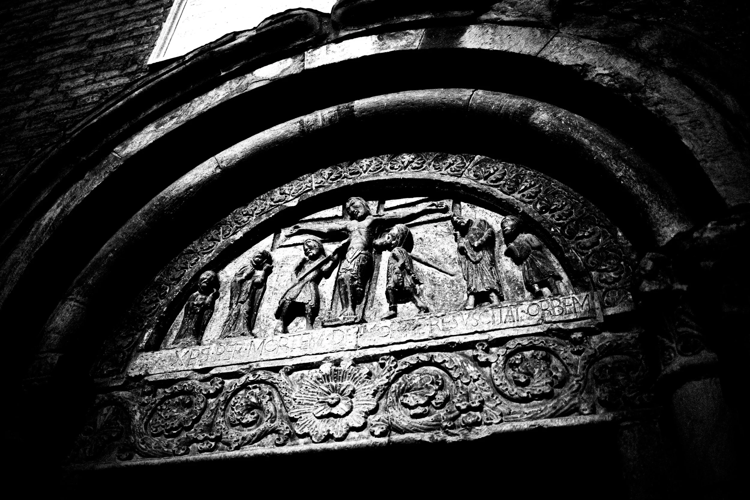 Scultura raffigurante la Crocifissione di Gesù, posizionata in un arco architettonico, decorata con motivi floreali