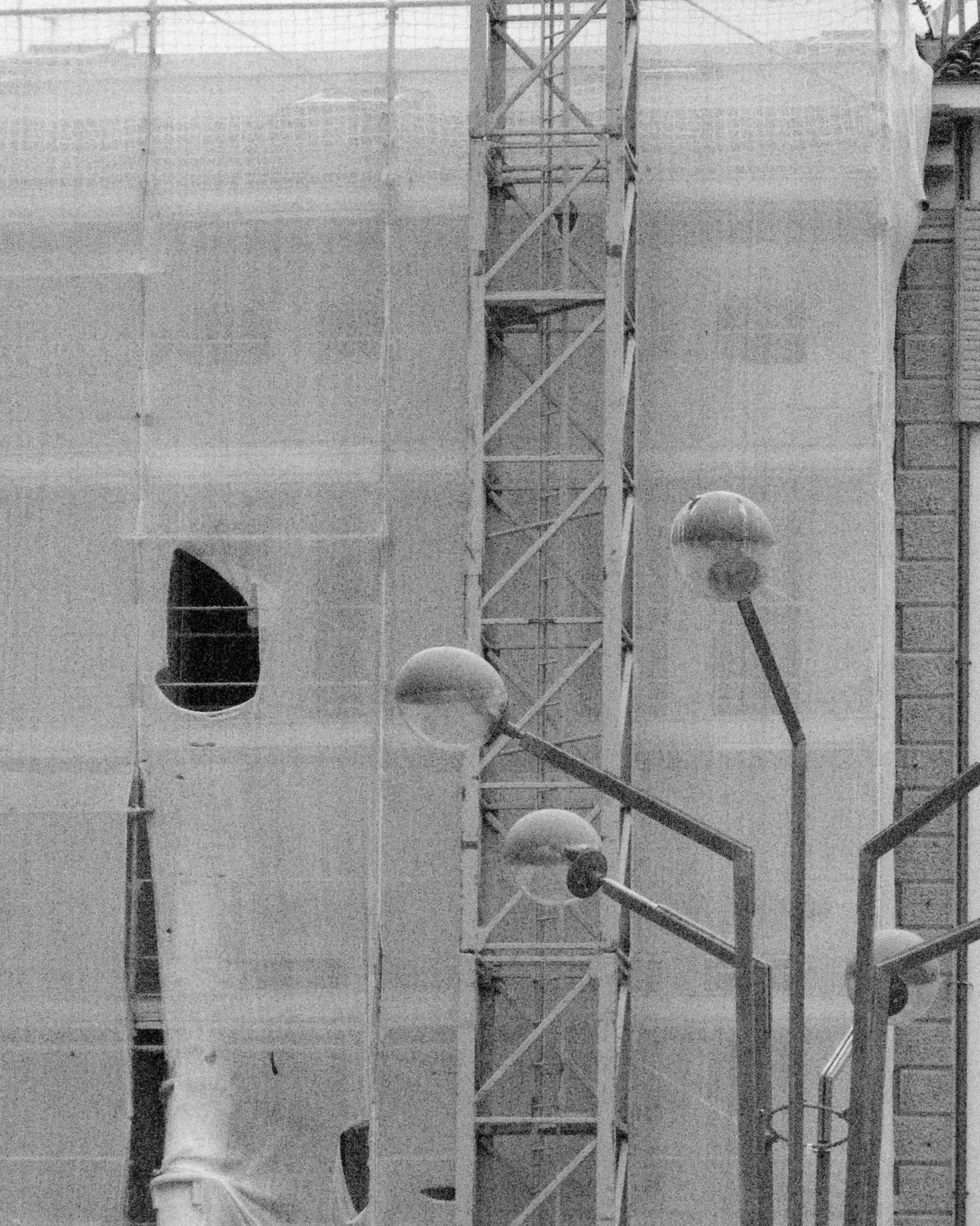 Immagine in bianco e nero di un cantiere o di un edificio in costruzione con componenti di struttura e lampioni.
