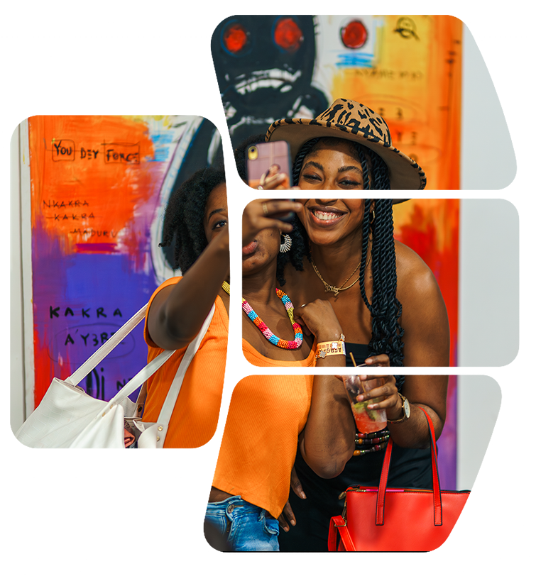 Two smiling women taking a selfie together at an art gallery, with colorful abstract artwork in the background. One woman is wearing an orange top, a beaded necklace, and a white handbag, while the other is wearing a leopard print hat, black dress, and holding a red handbag and a drink.