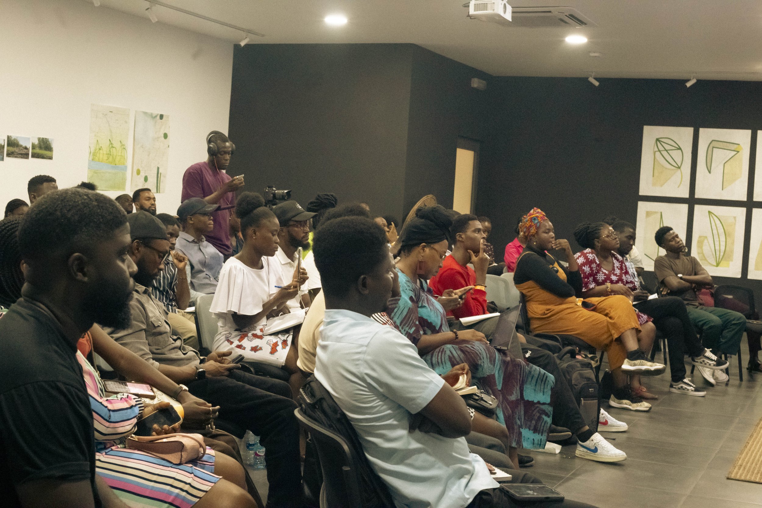 An audience of diverse people sitting and listening in a conference room with artwork on the walls.