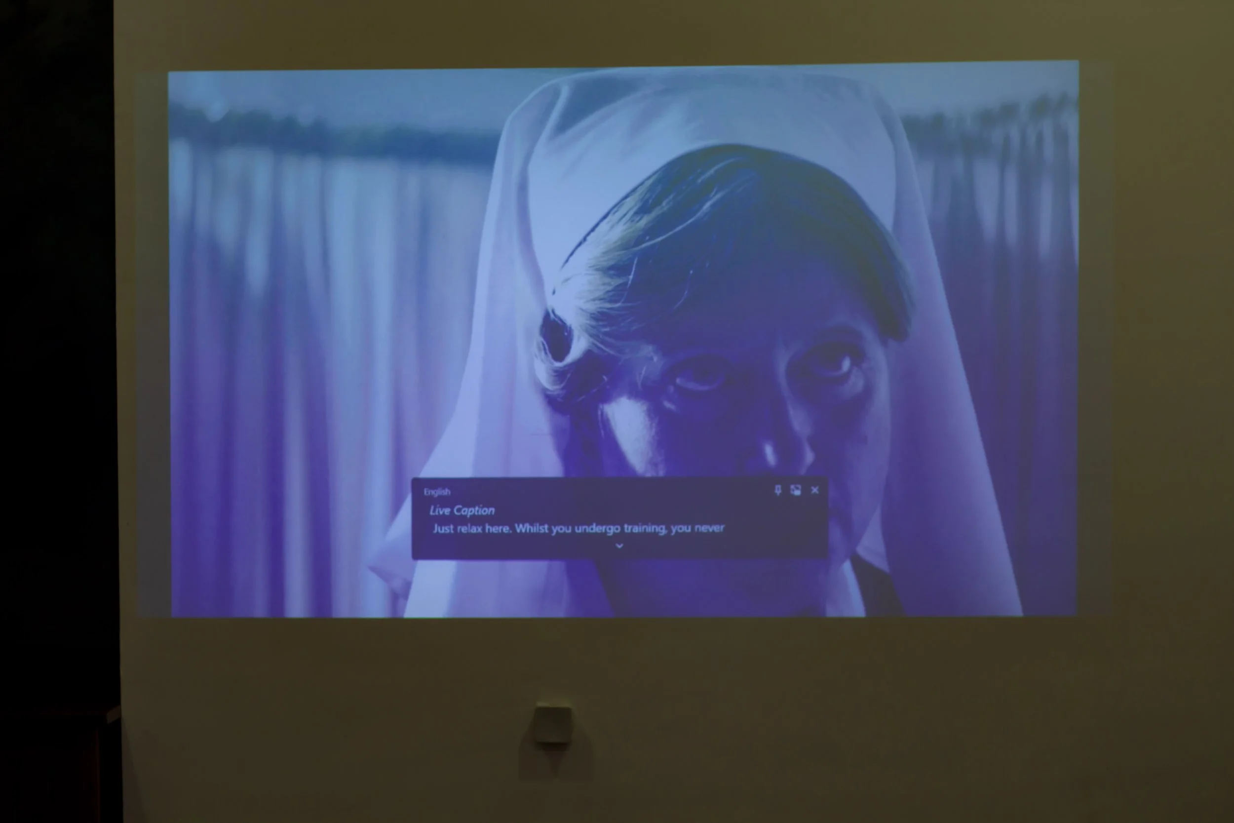 Projected image of a statue of a woman with a veiled head, with a speech bubble that says, "Just relax here. Whilst you undergo training, you never".