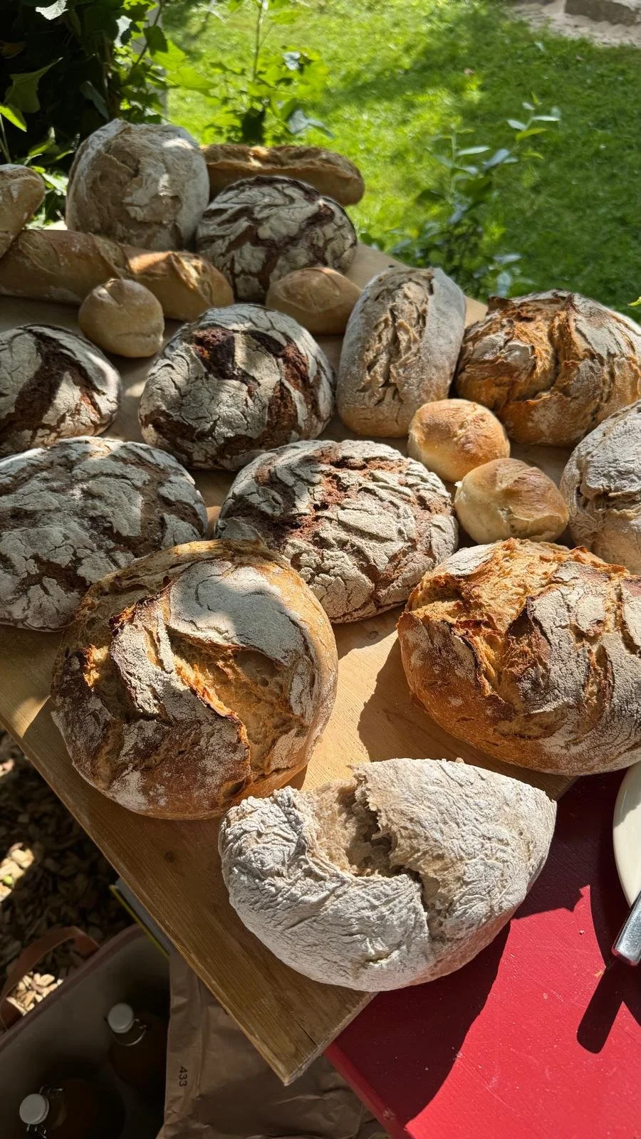 Verschiedene frisch gebackene Brote und Brötchen auf einem Holzbrett im Freien.