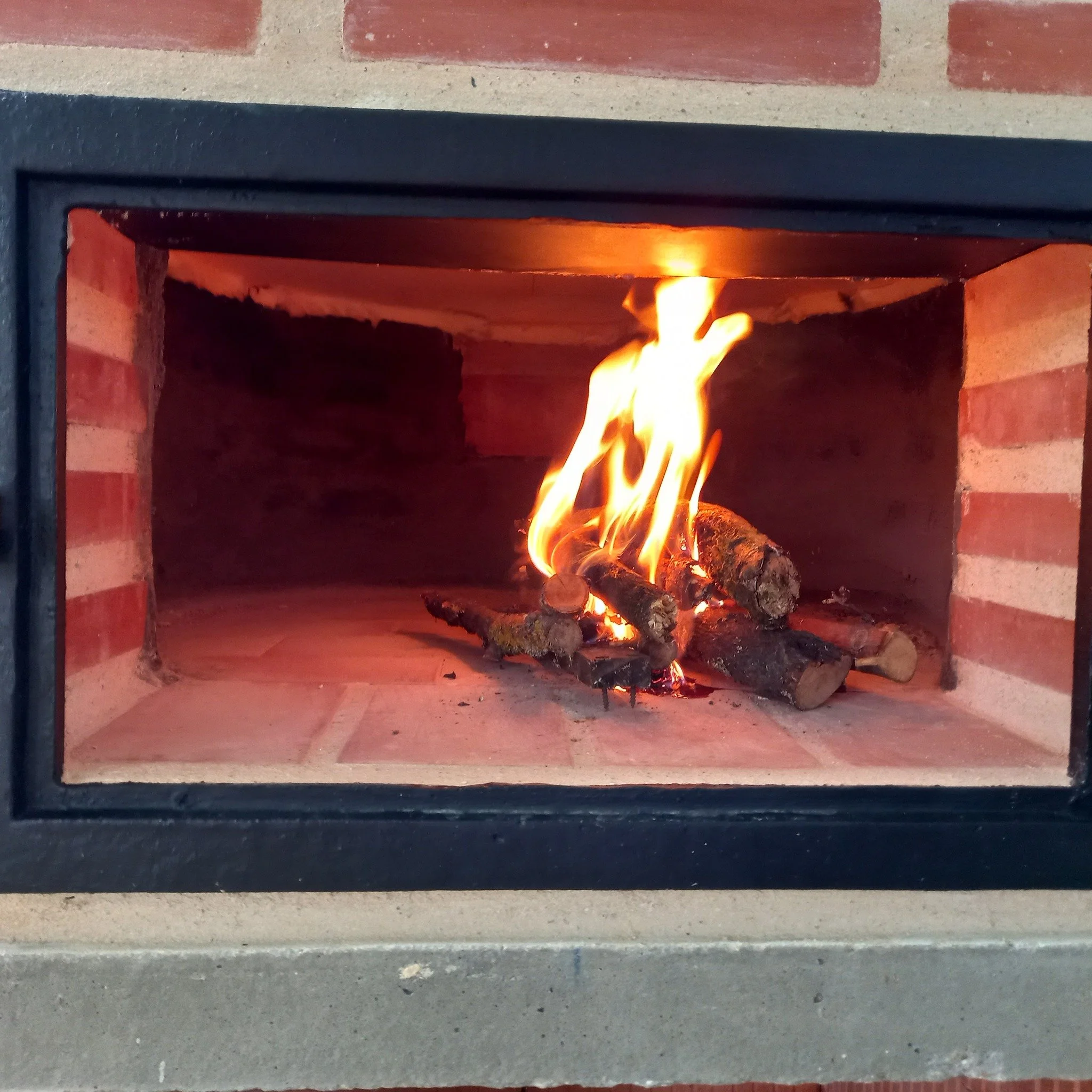 Brennender Kamin mit Holzscheiten in einem gemauerten Feuerraum.
