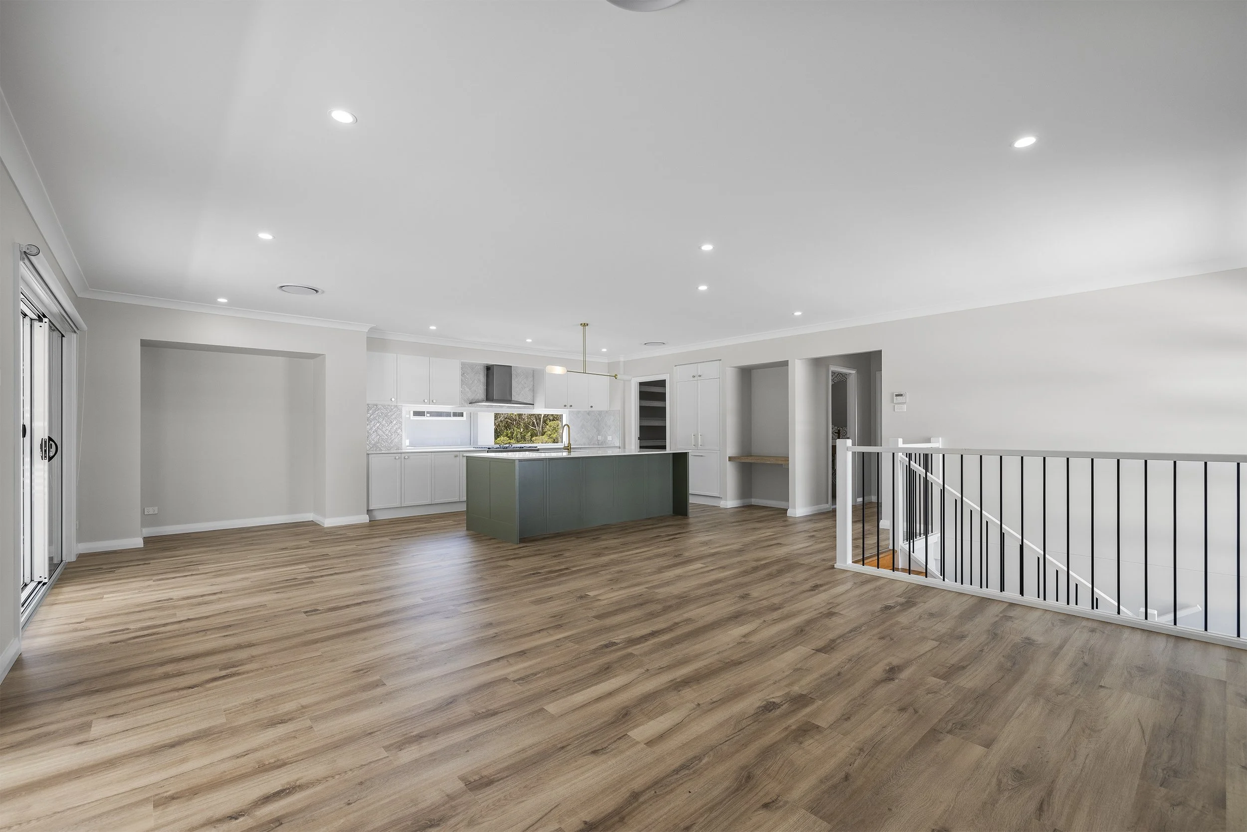 Empty open-concept living space with hardwood floors, white walls, a kitchen with white cabinets, a green kitchen island, and large sliding glass doors.