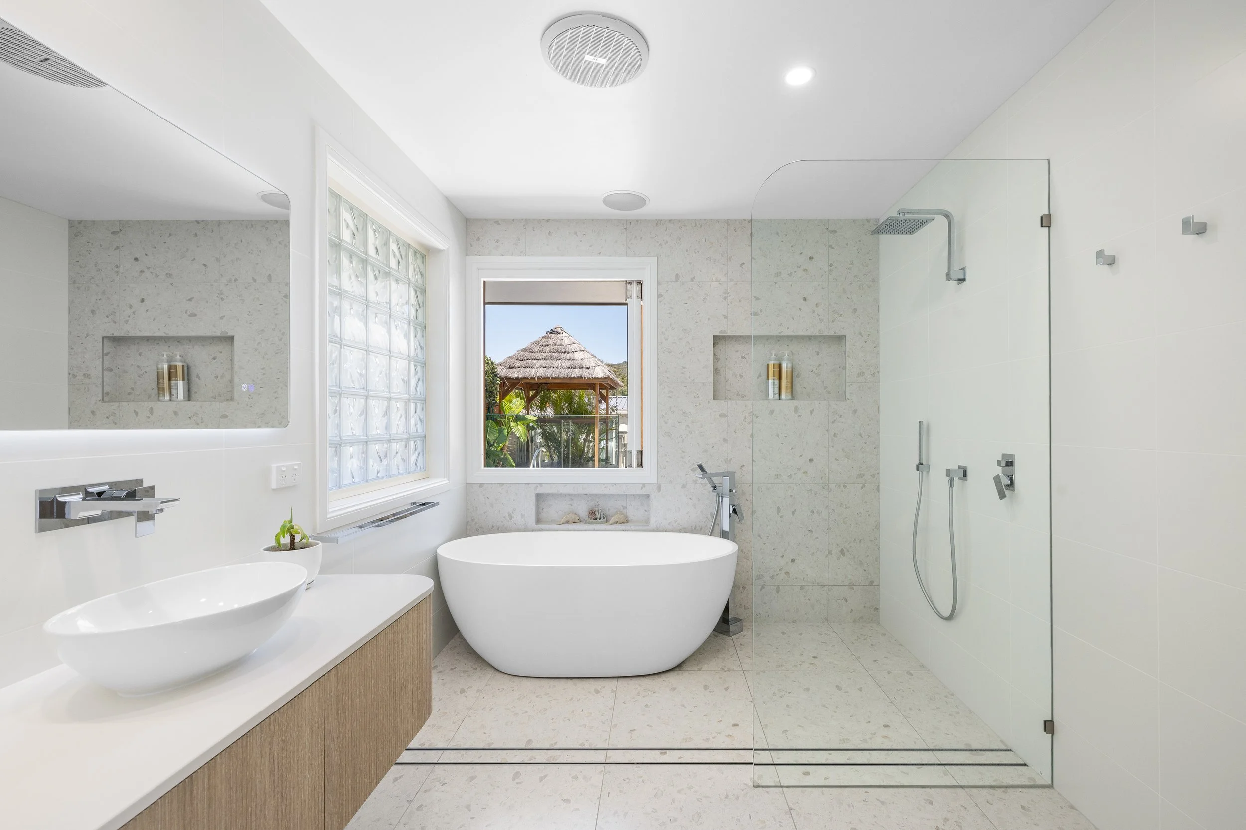 Modern bathroom with a freestanding bathtub by a window, a glass shower enclosure, a white vanity with a vessel sink, and a large mirror.