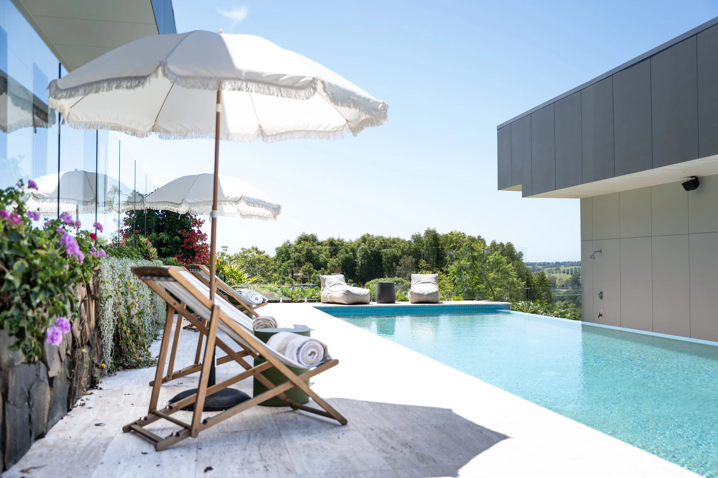 Luxury outdoor swimming pool with lounge chairs, umbrellas, and a scenic view of trees and hills.