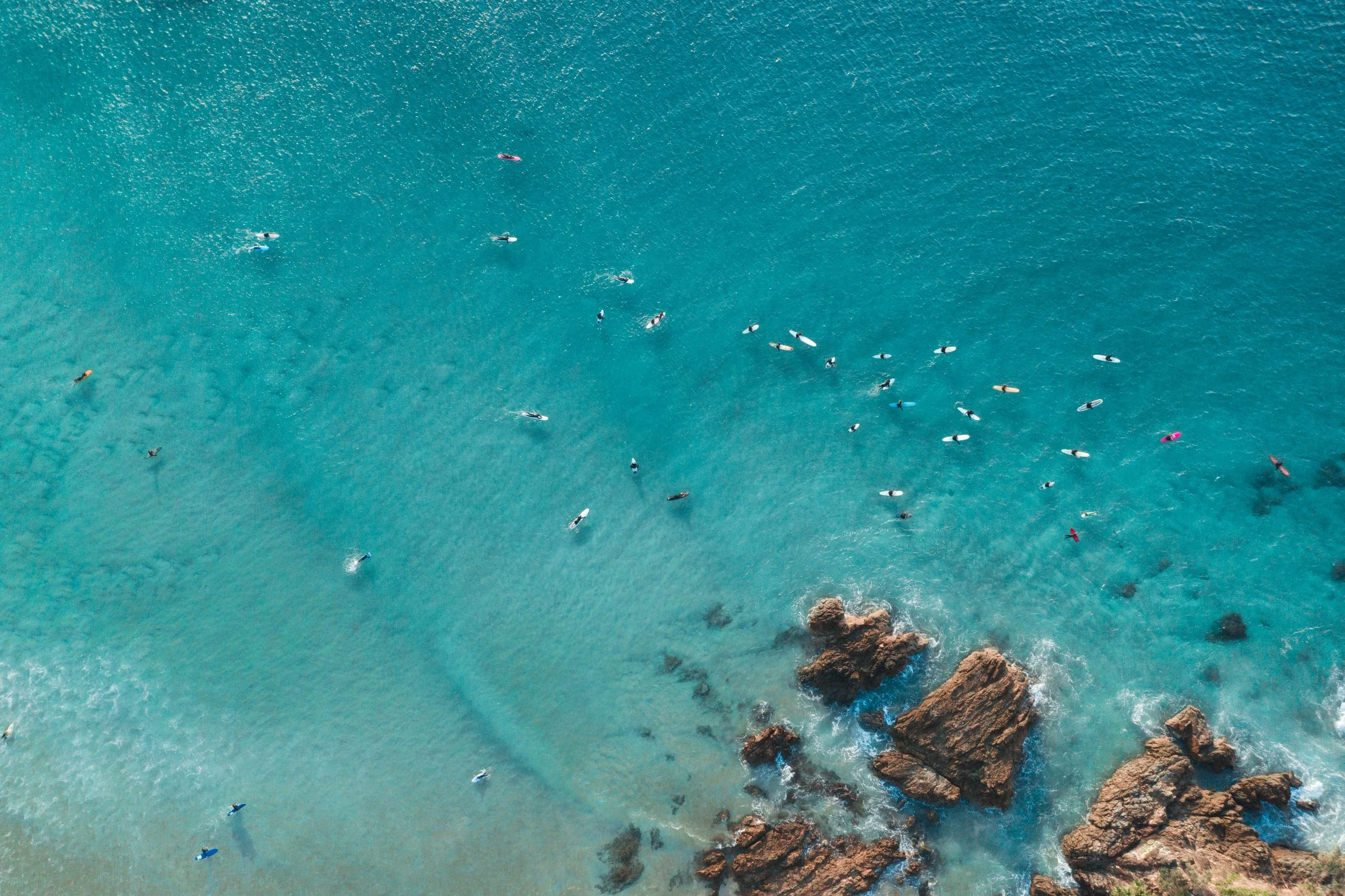 Byron Bay coastal drone photography for real estate advertising capturing an aerial view of a group of surfers in the ocean near a rocky shoreline surf break called The Pass.