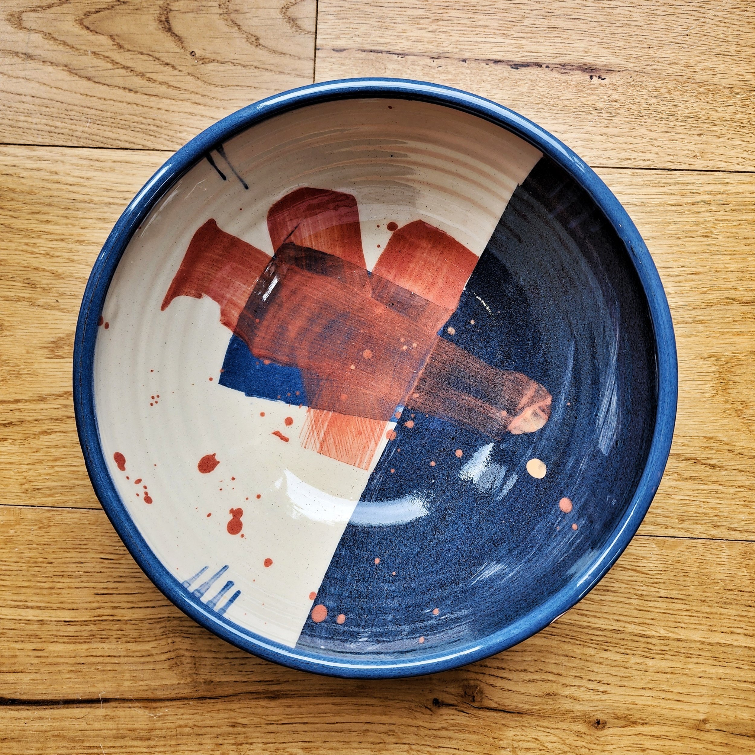 Decorative ceramic plate with abstract red, white, and dark blue paint streaks, placed on a wooden surface.