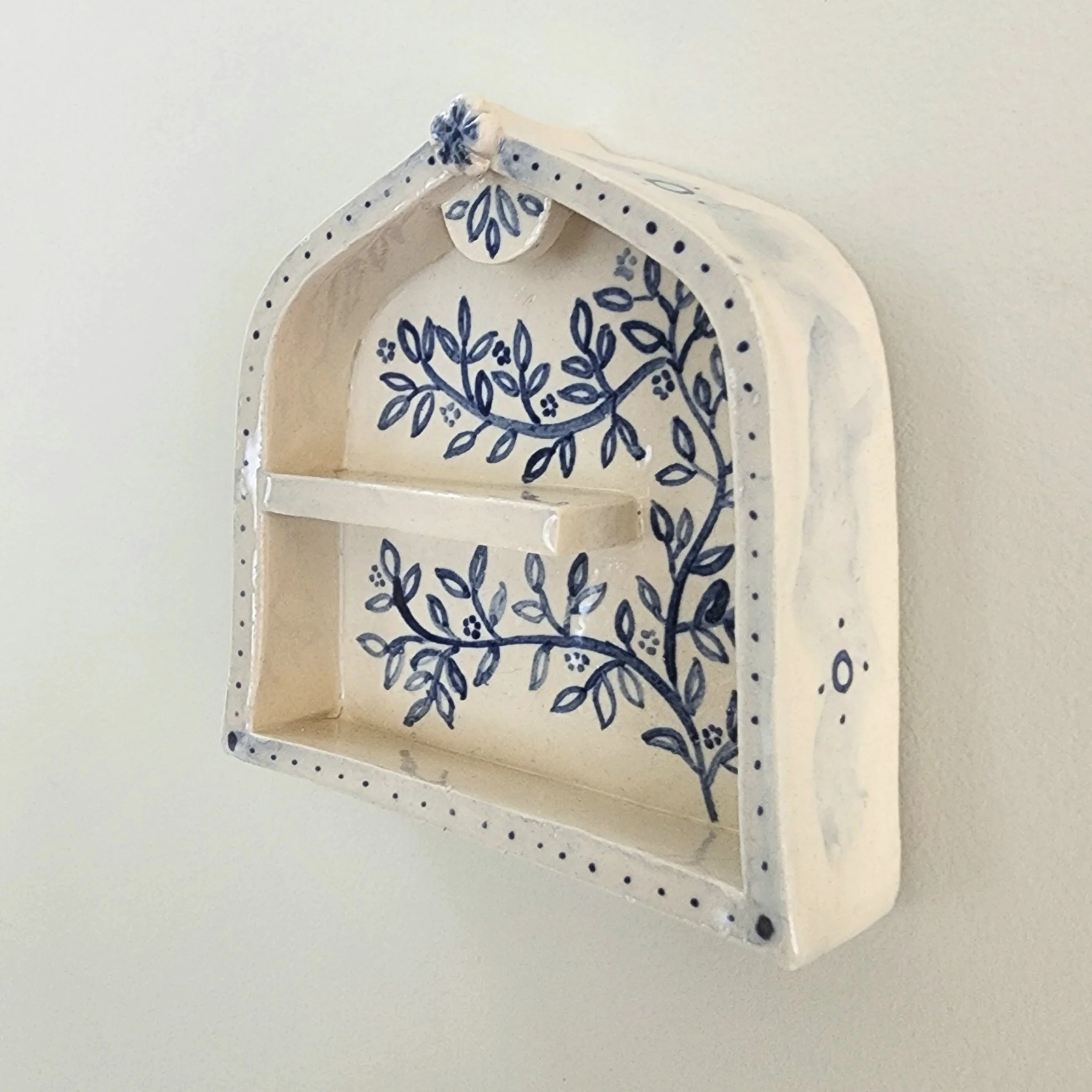 One-off wall hung shrine in stoneware. Hand painted and then glazed. Hangs on a nail. 

The illustrations are inspired by sketches of flowers in my garden. 

Can be used to display small trinket, or just hang as is. 

Measurements:
Height: 9cm
Width: