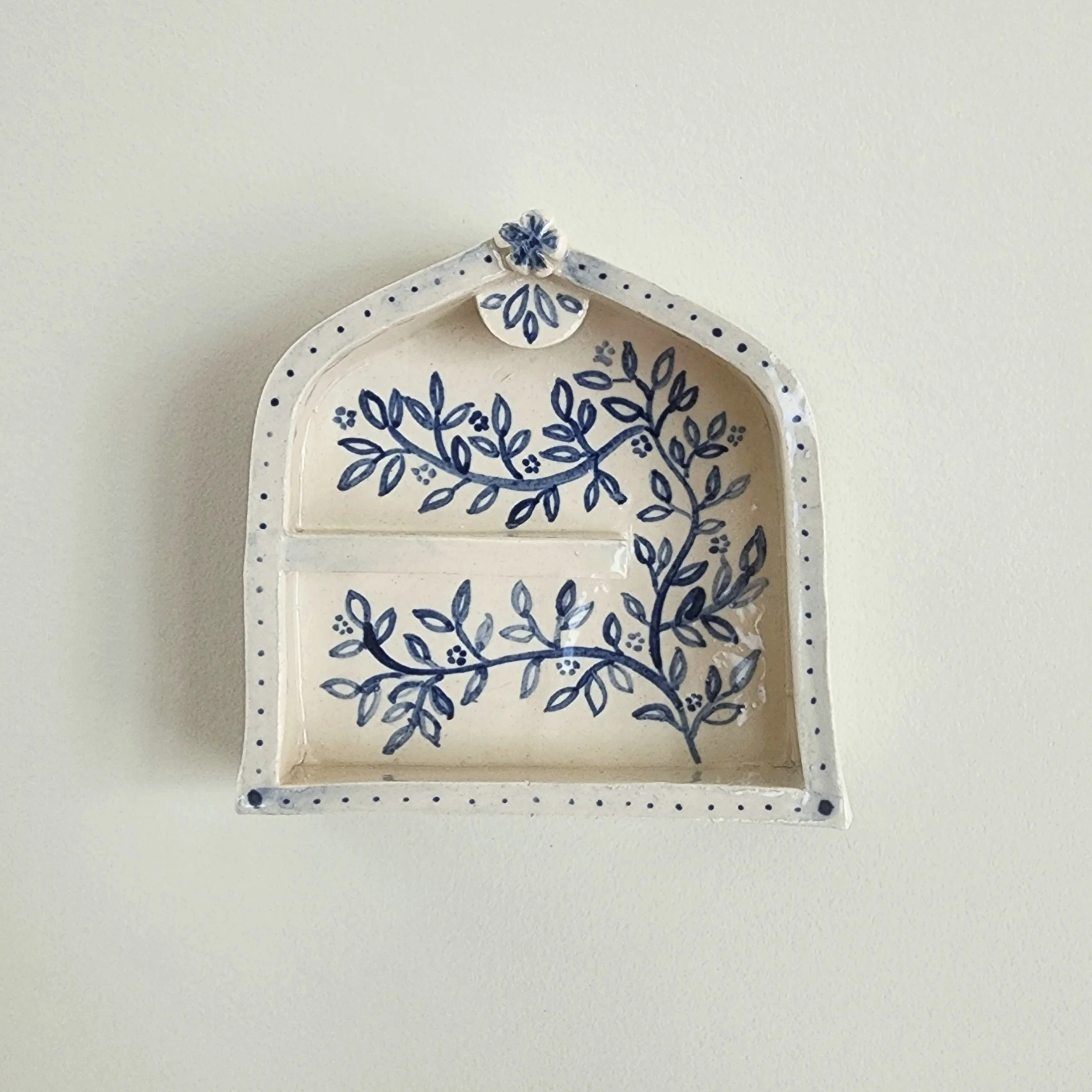 One-off wall hung shrine in stoneware. Hand painted and then glazed. Hangs on a nail. 

The illustrations are inspired by sketches of flowers in my garden. 

Can be used to display small trinket, or just hang as is. 

Measurements:
Height: 9cm
Width:
