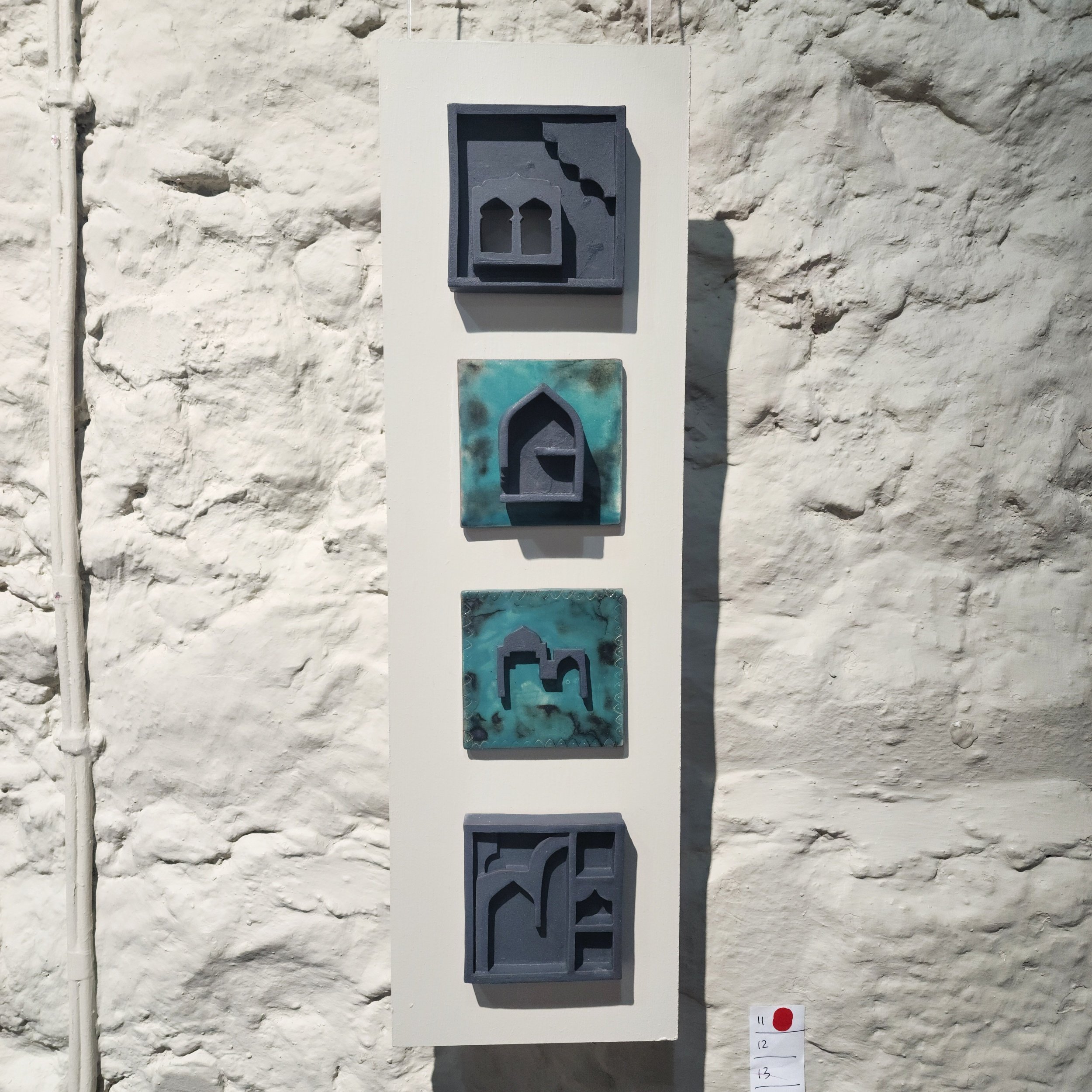 Set of four decorative tiles with abstract geometric designs mounted on a white wall.