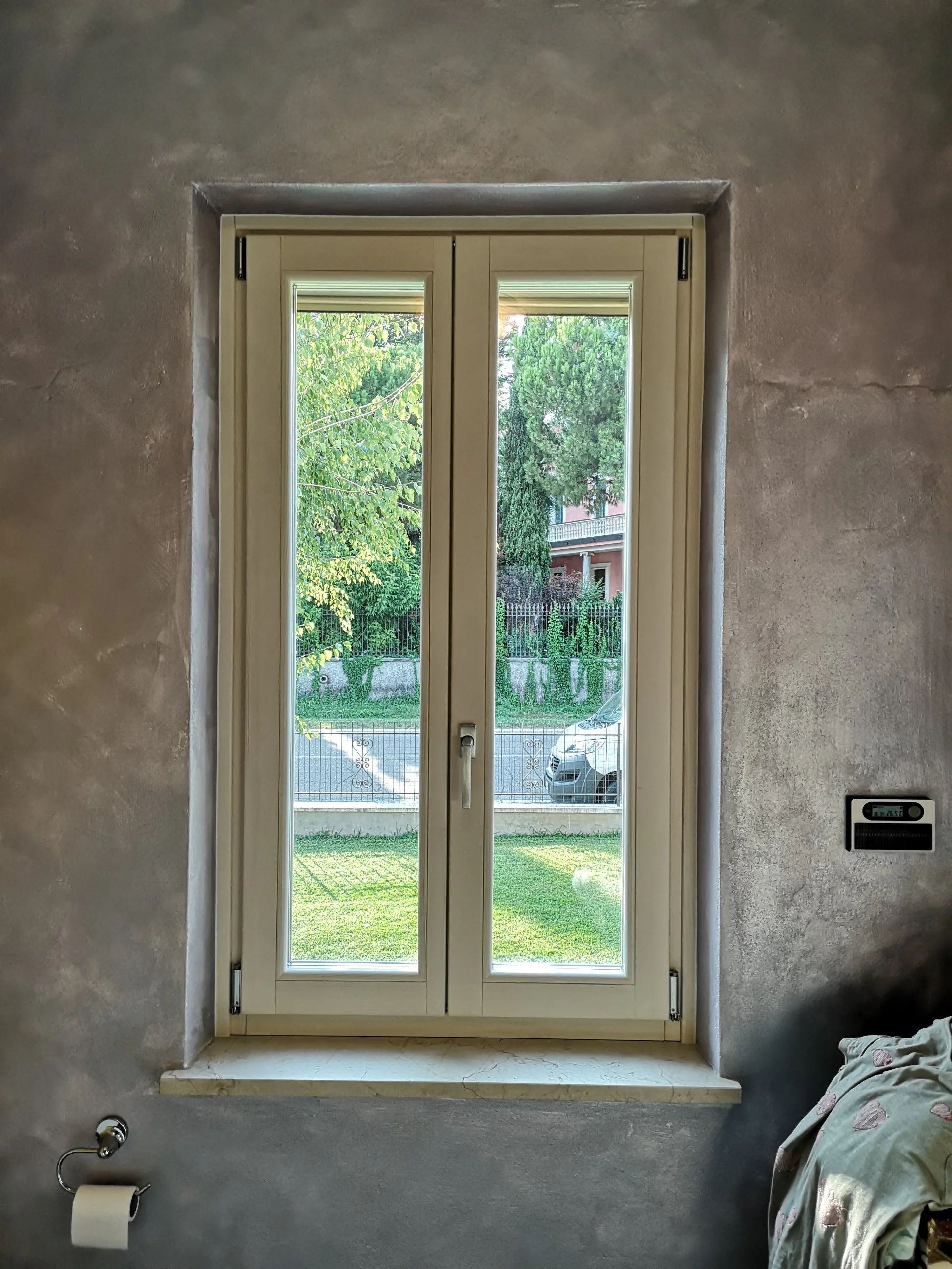 Finestra bianca con vetri e vista su giardino verde e strada esterna, con muschio sulle pareti interne