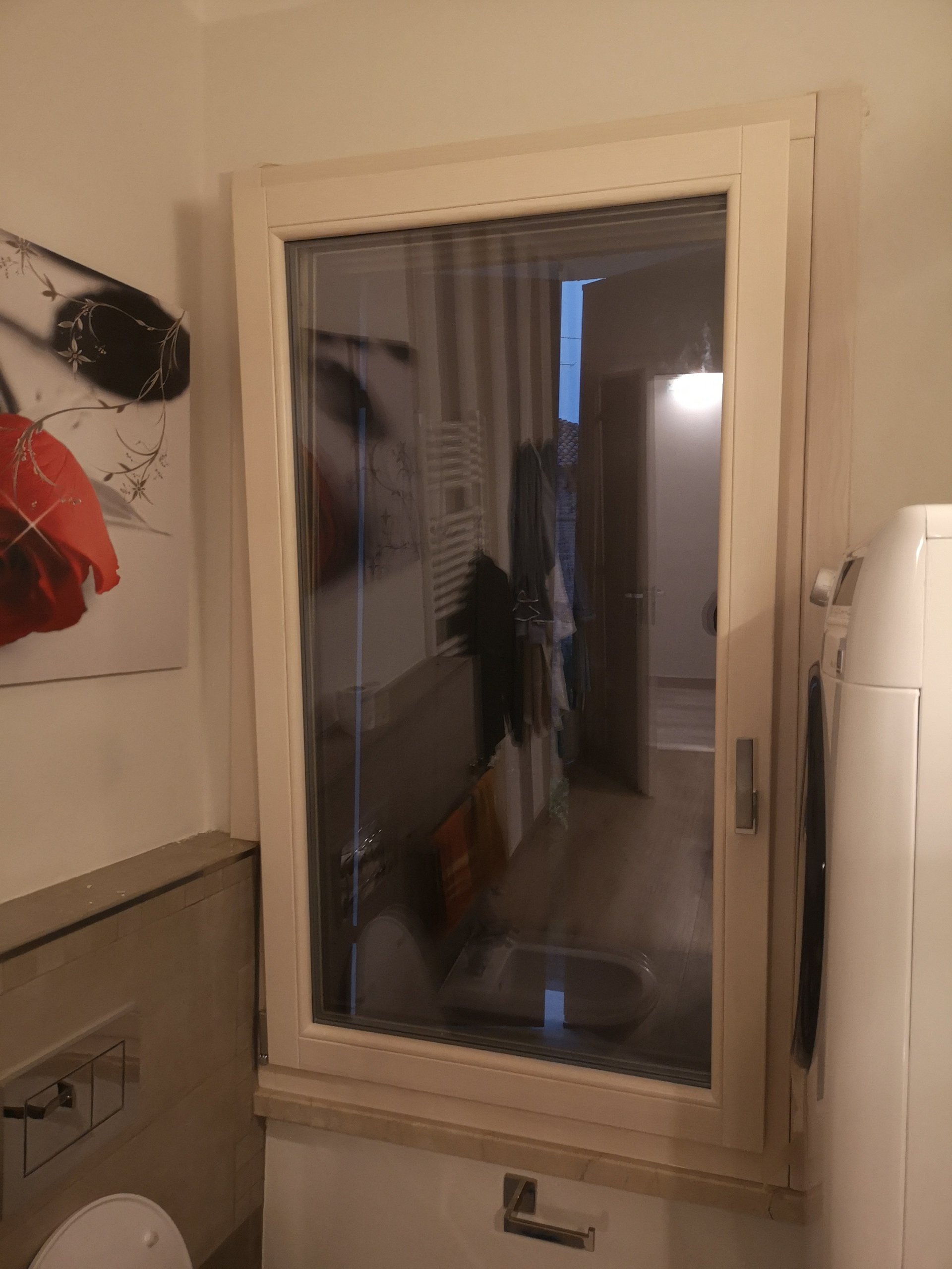 Una porta finestra a vetri che separa un bagno da un'altra stanza, con vestiti appesi visibili attraverso il vetro.