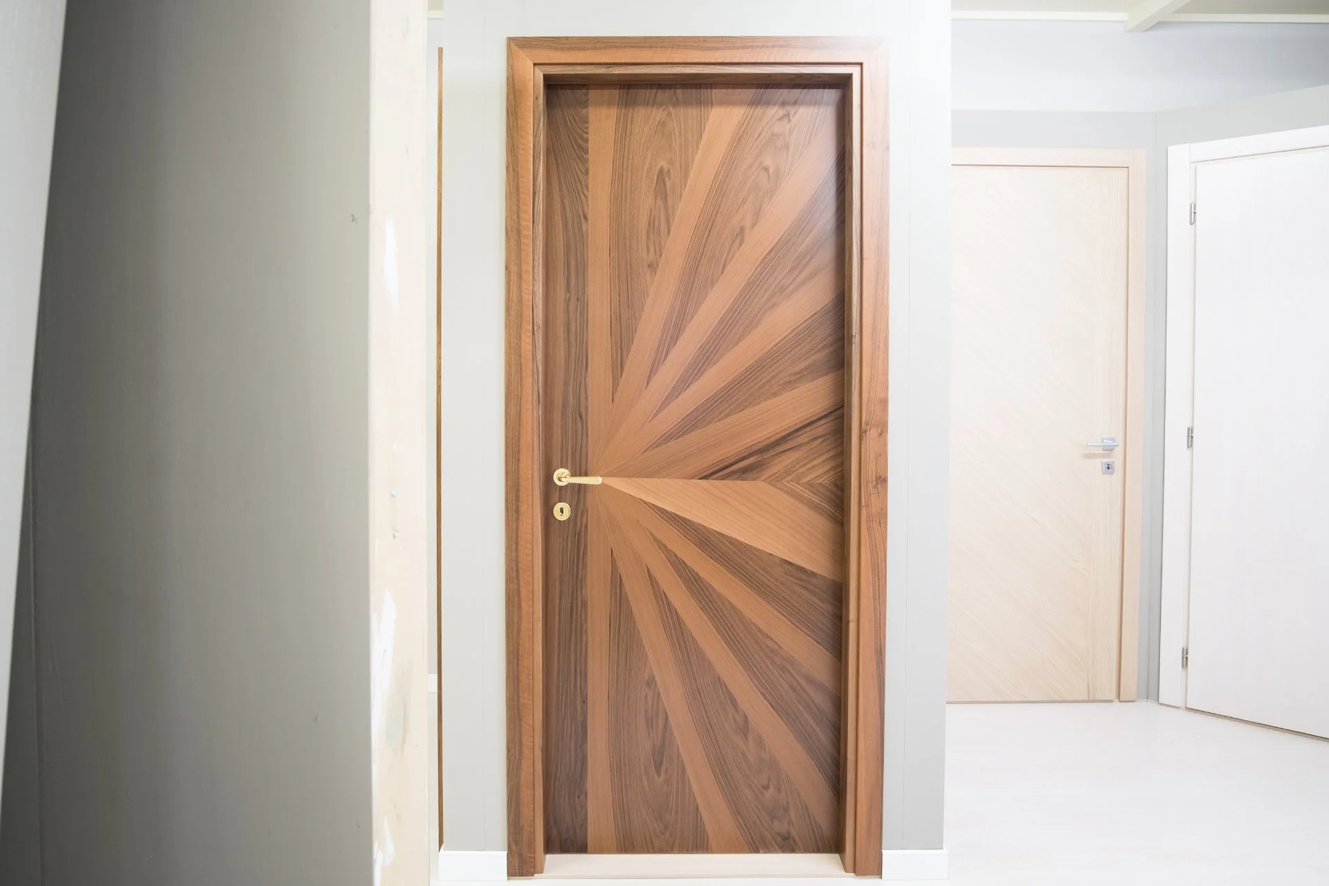 Porta in legno con motivo geometrico a raggi di colore marrone scuro e chiaro, con maniglia dorata.