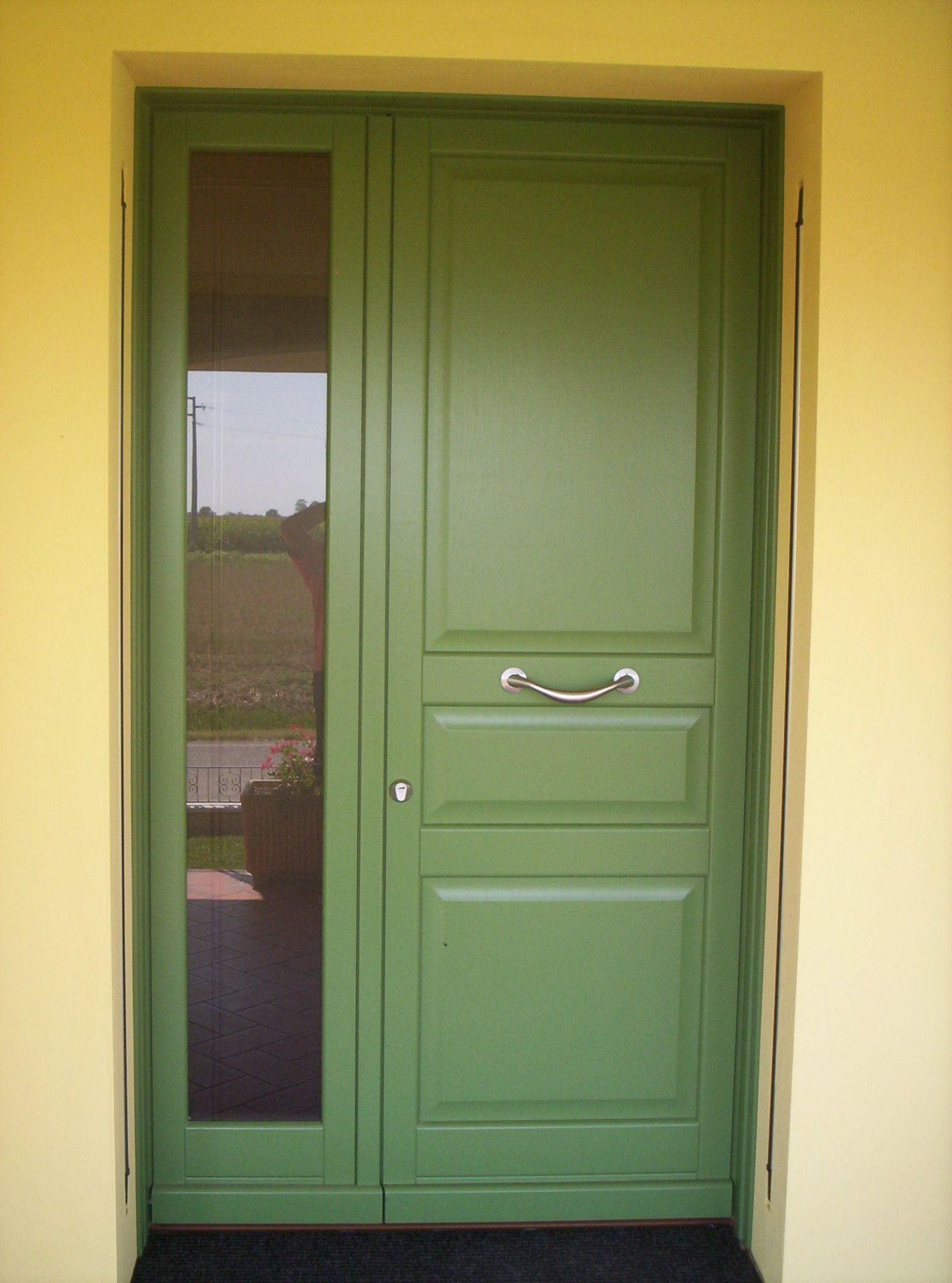Porta verde con vetro laterale, incastonata in una parete gialla.