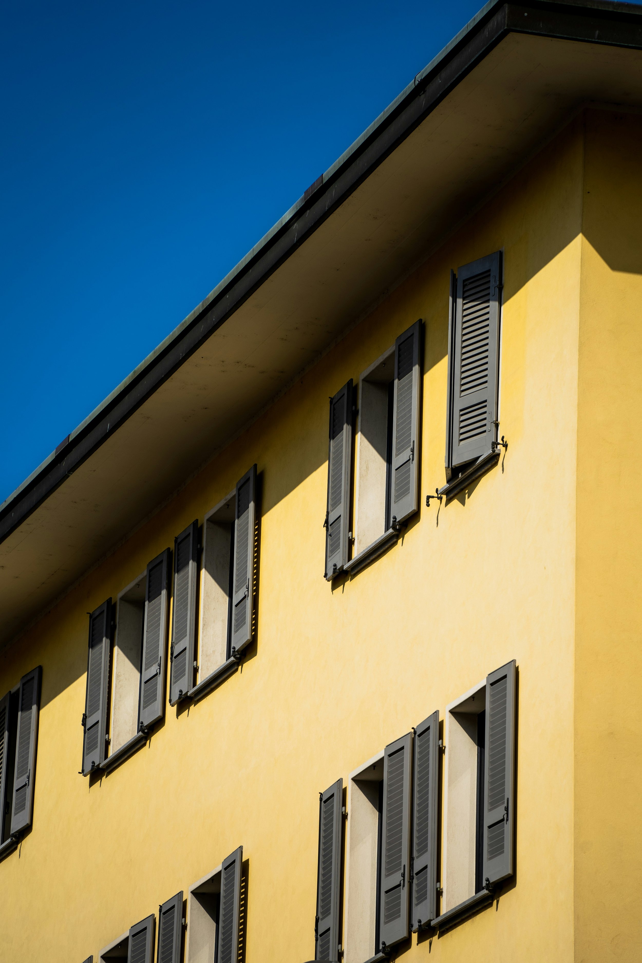 Edificio giallo con finestra e persiane nere sotto un cielo blu.
