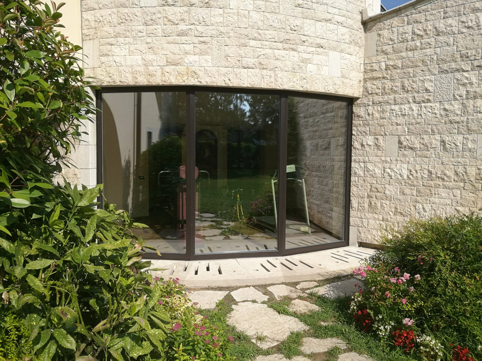 Veranda con finestre in vetro e struttura metallica, circondata da piante e fiori nel giardino