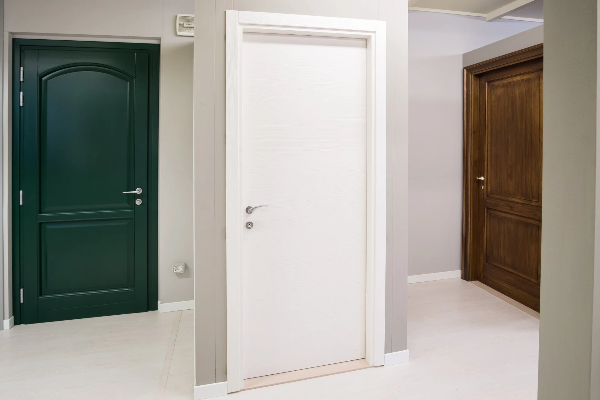 Tre porte interne, una verde, una bianca e una in legno, in un ambiente domestico con pareti grigie e pavimento chiaro.