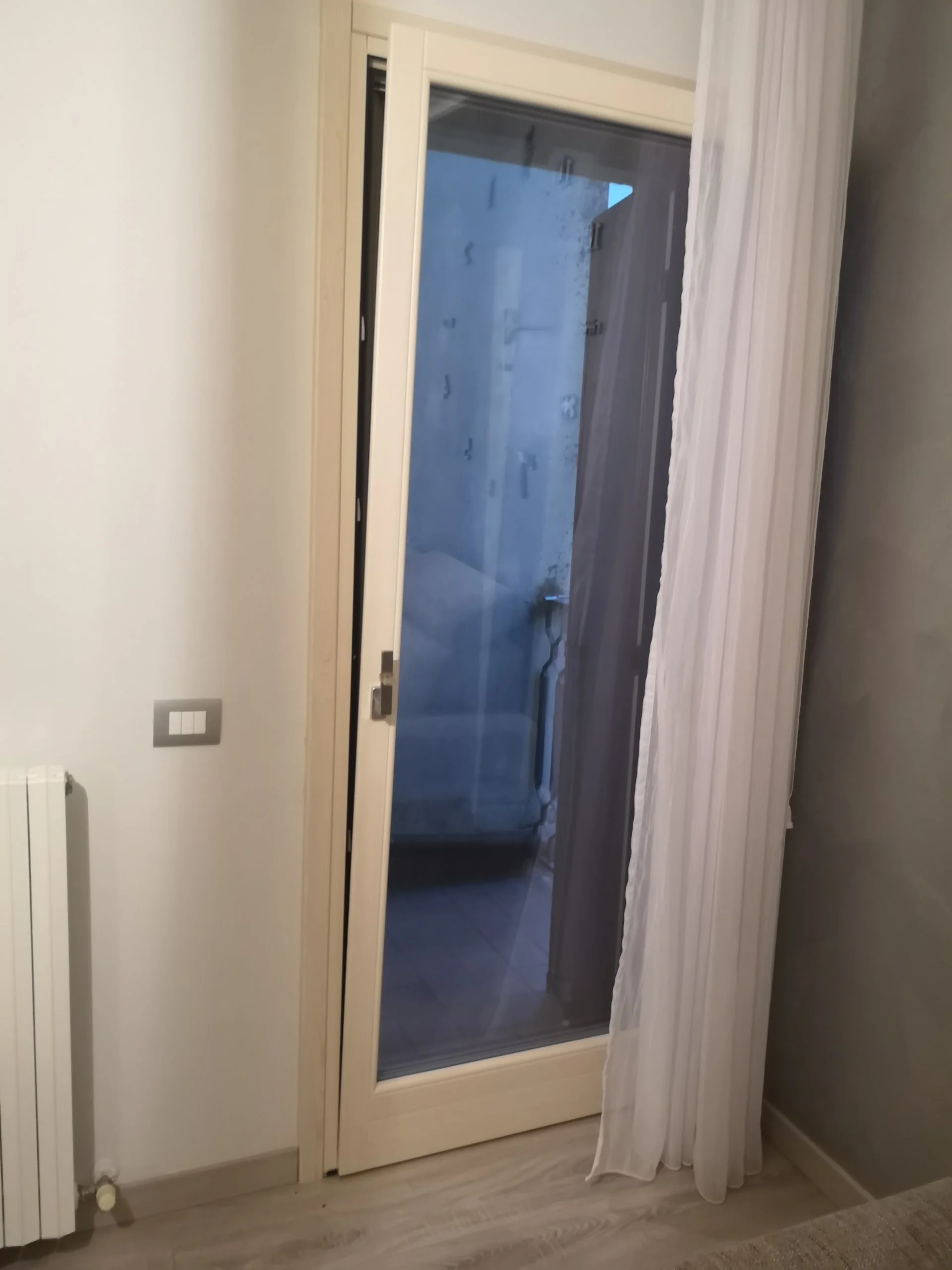 Porta finestra scorrevole con tende bianche in una stanza domestica.