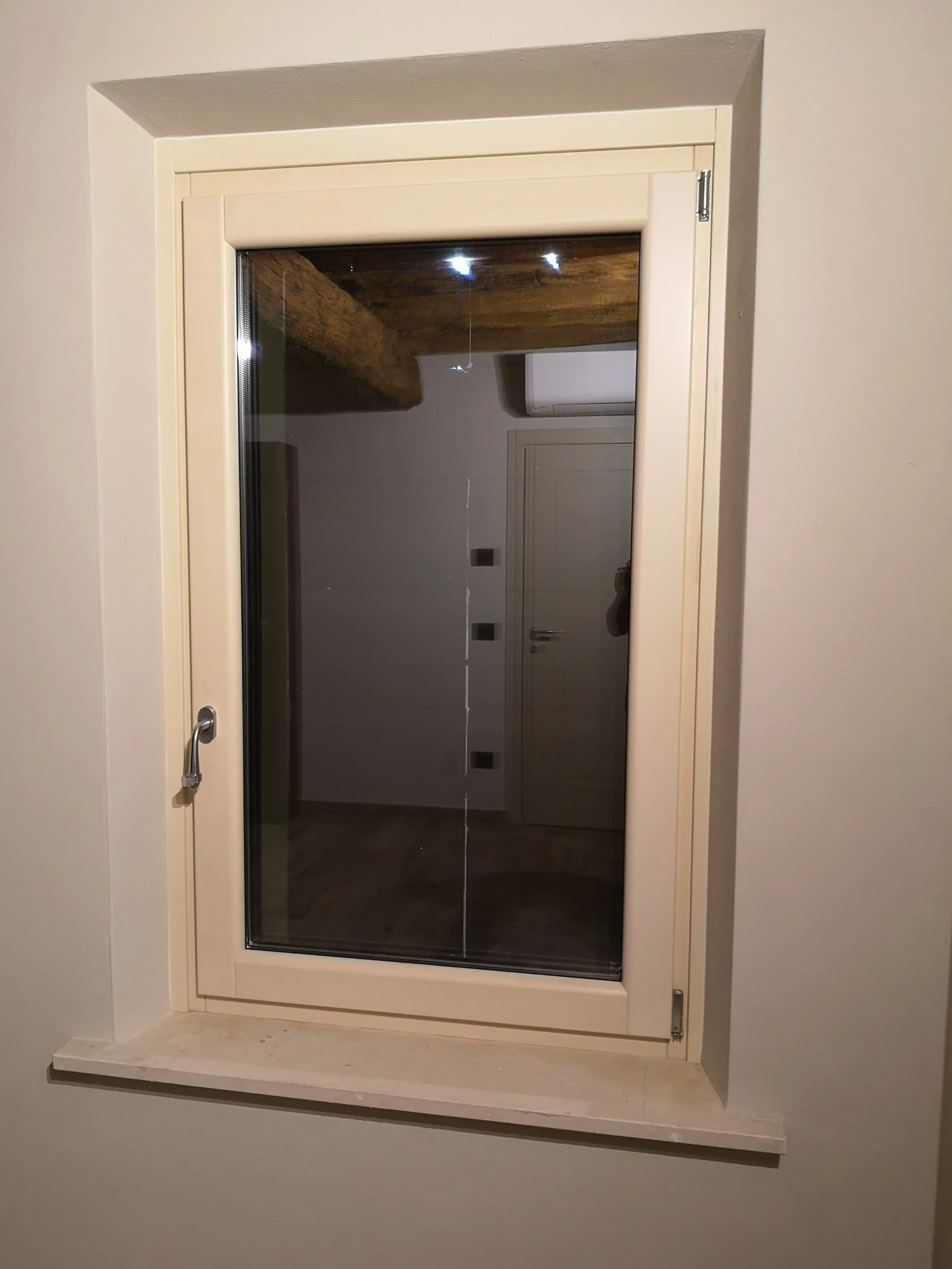 Finestra con cornice beige e vetro, installata in una parete, con vista sull'interno di una stanza.
