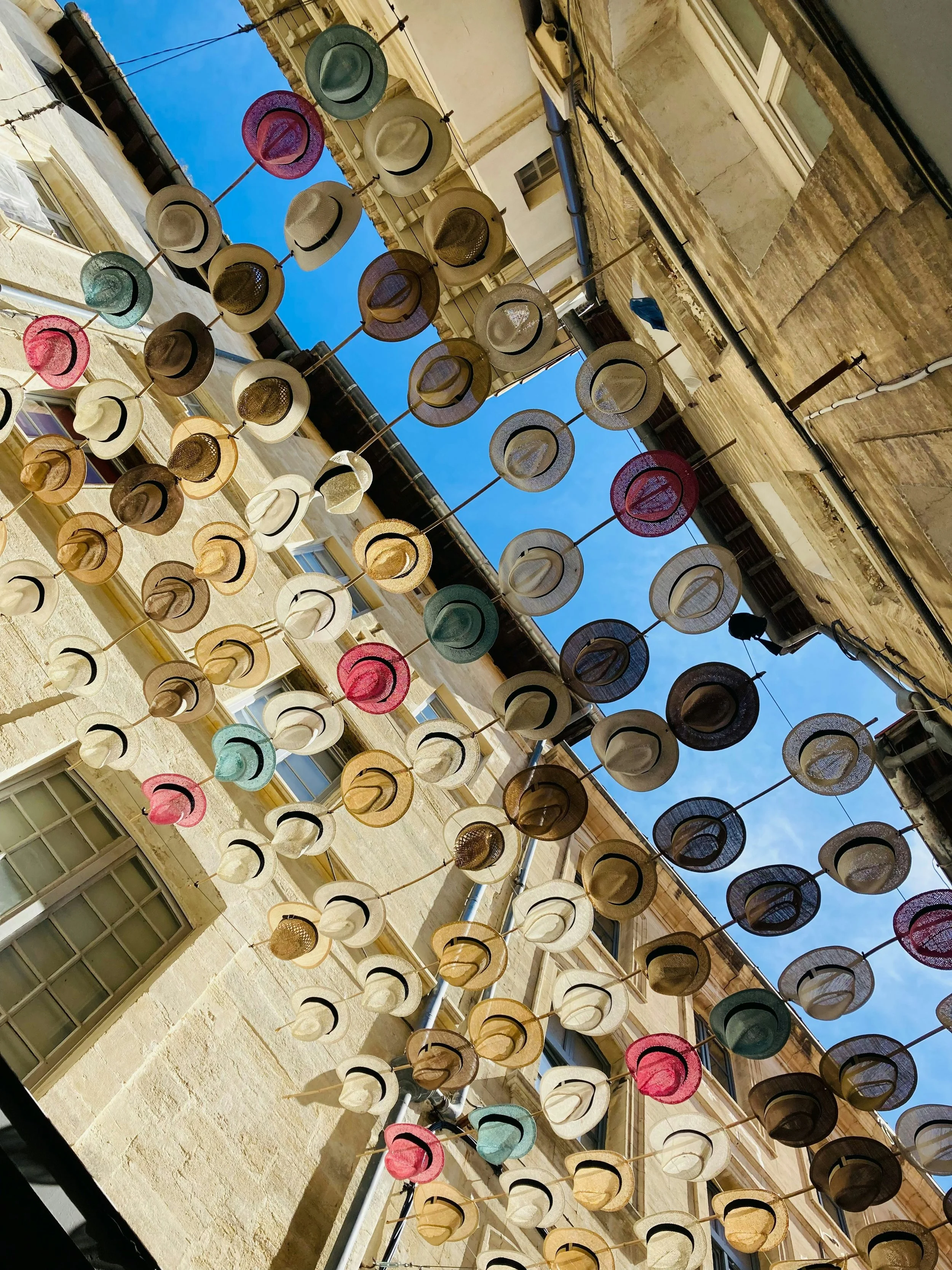 Installation artistique de chapeaux suspendus dans une rue d’Avignon, symbolisant l’ambiance estivale et culturelle de la Provence.
