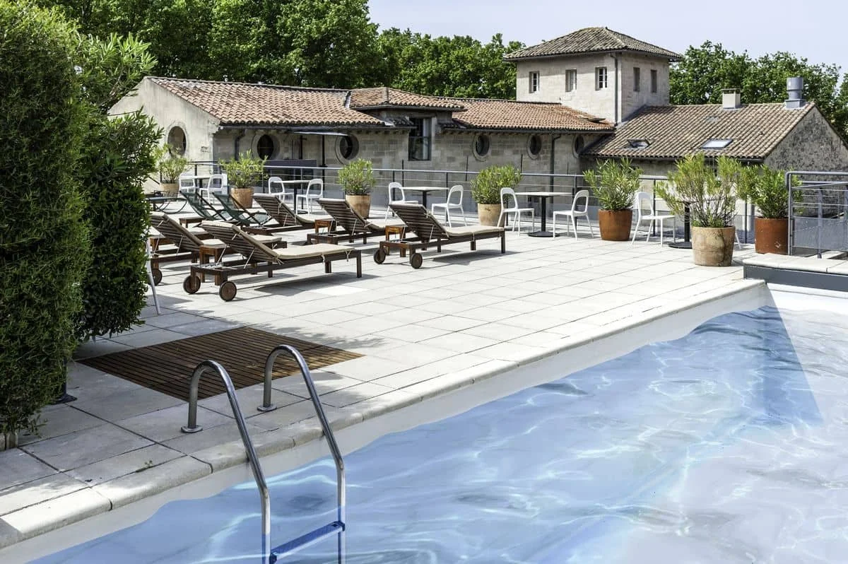 Piscine extérieure de l'Hôtel Le Cloître Saint-Louis, entourée de transats, offrant un espace de détente après un séminaire