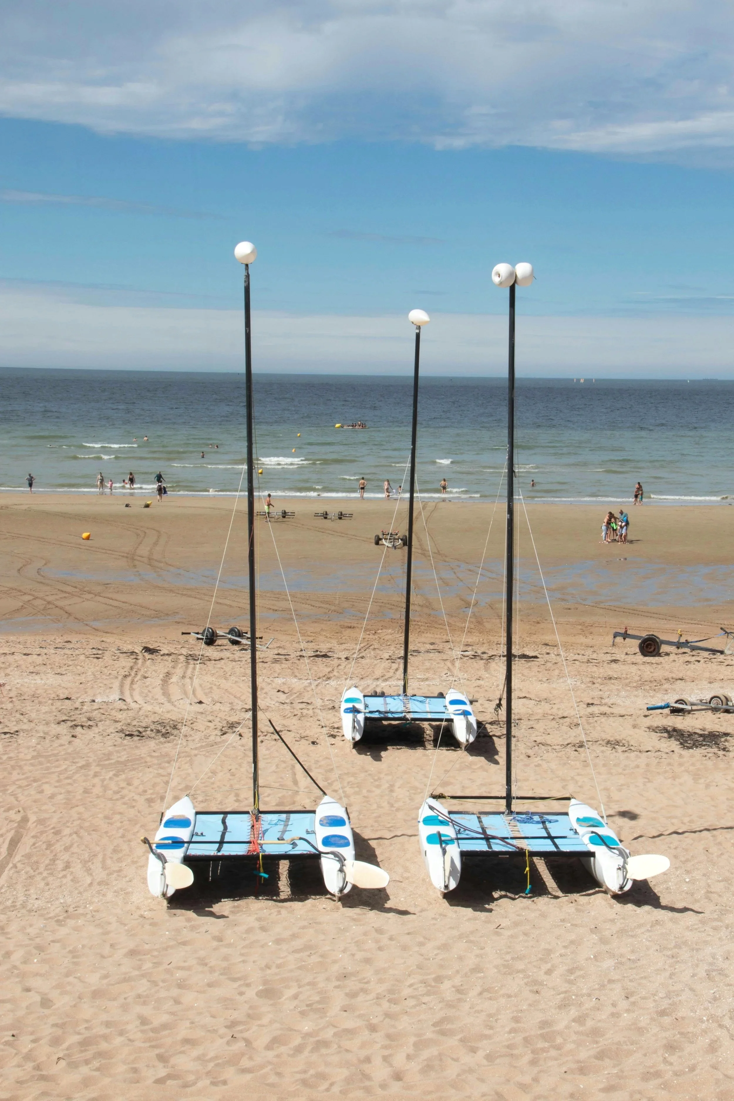 trois char à voile prêts à porter sur la large plage de sable de Cabourg. La scène montre des familles profitant d’activités et de sports en mer sous un ciel dégagé.