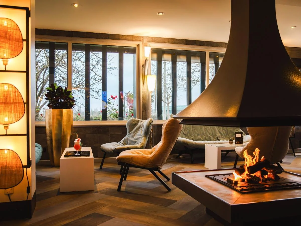Salon de l’hôtel Mercure Cabourg avec une cheminée centrale moderne et des fauteuils design. L’espace est accueillant et élégant, idéal pour la socialisation des invités.