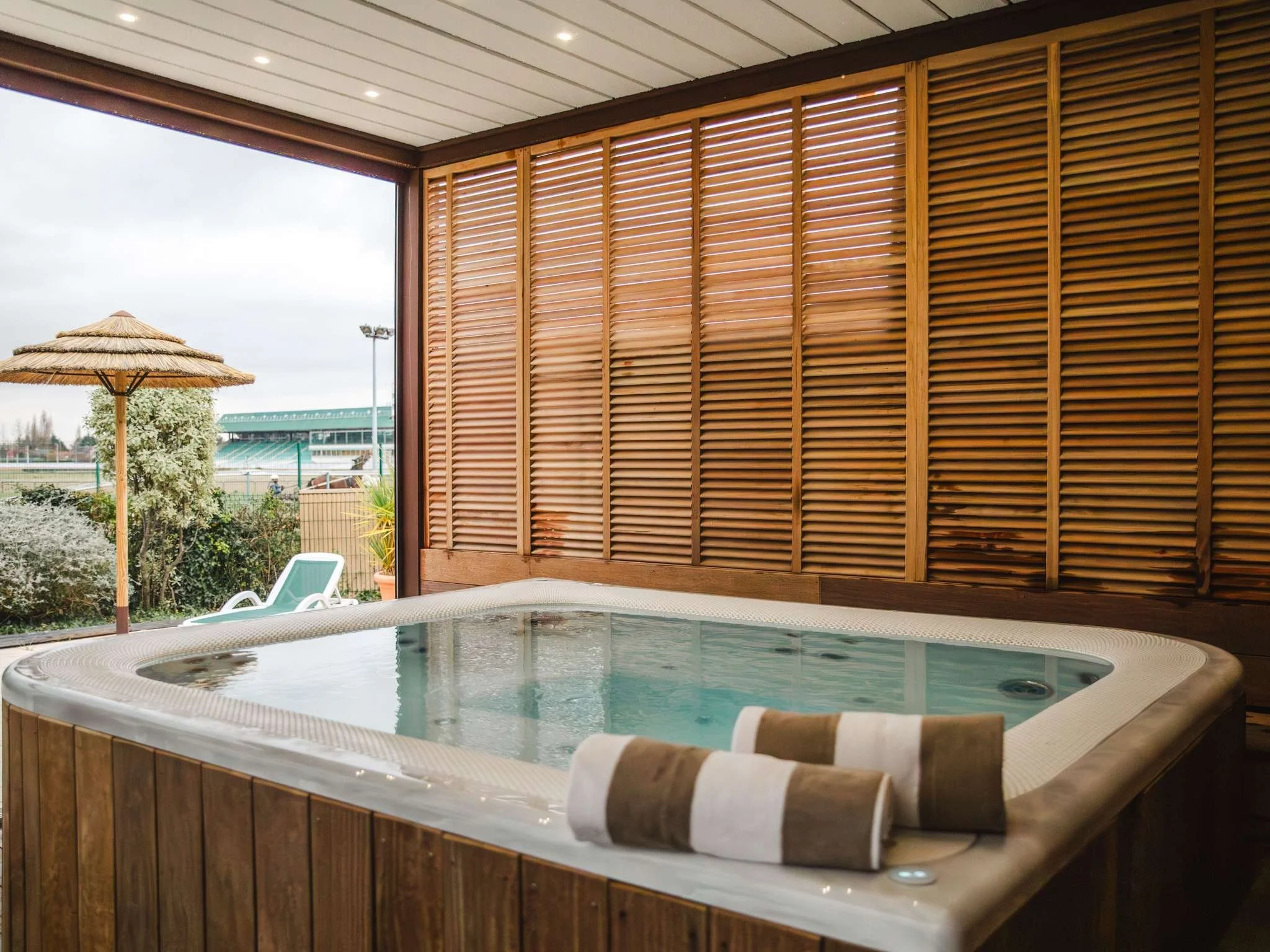 Jacuzzi extérieur à l’hôtel Mercure Cabourg, entouré d’une clôture en bois pour plus d’intimité. L’espace spa est idéal pour la détente.