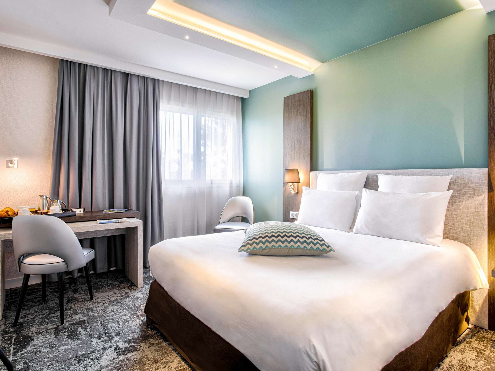 Chambre d’hôtel à l’hôtel Mercure Cabourg avec un design moderne et fonctionnel, grand lit avec tête de lit blanche et bureau. L’espace est lumineux et simple.