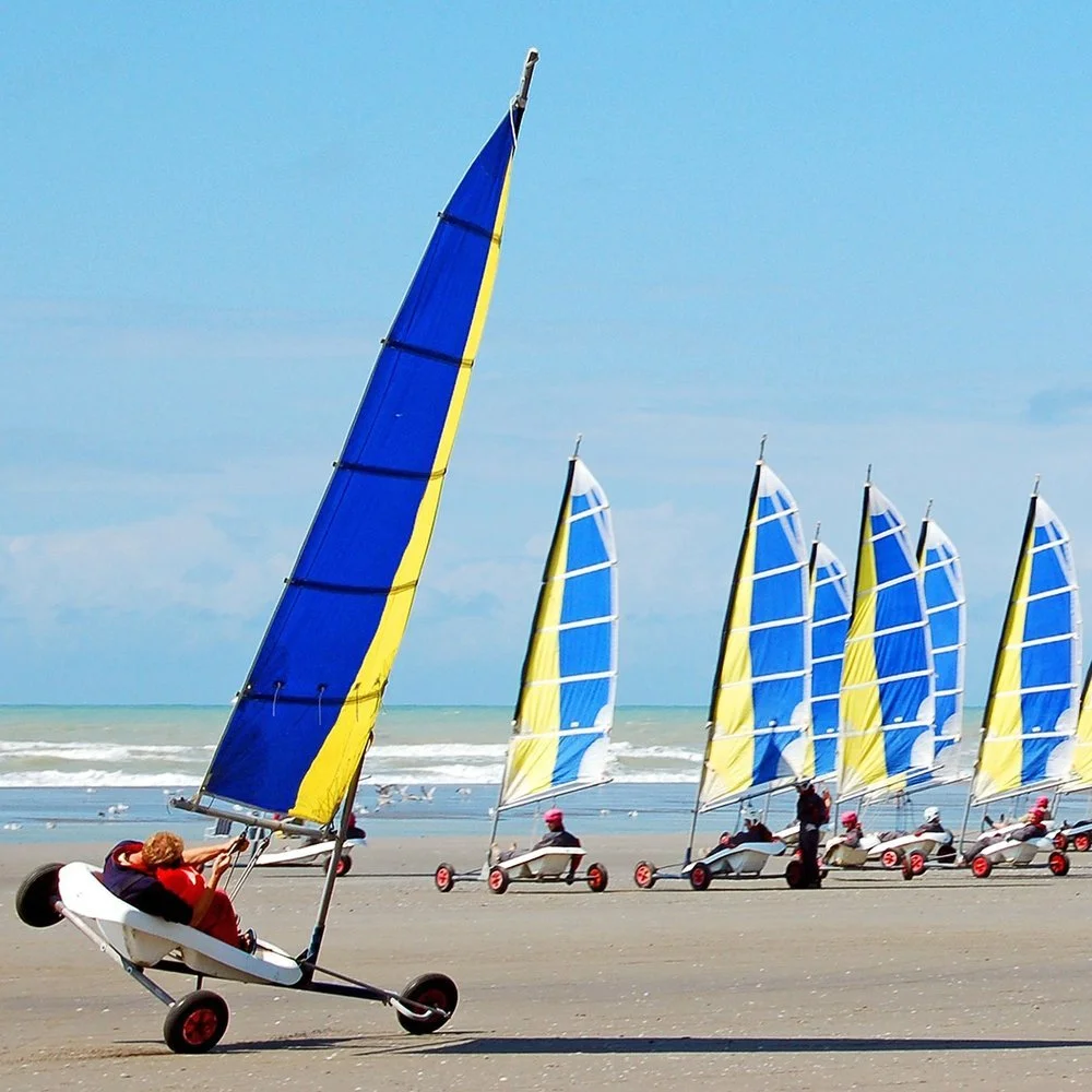 char à voile avec des voiles bleues et jaunes glissant sur la plage de Cabourg. L’image montre une activité palpitante et côtière.