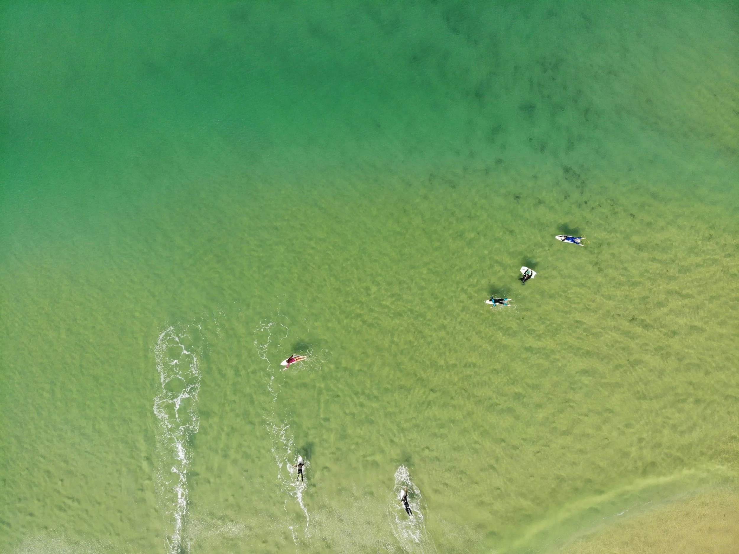 Vue aérienne des surfeurs attendant les vagues dans les eaux peu profondes de la côte de Biscarrosse. L’eau vert émeraude montre le fond sablonneux de l’océan.