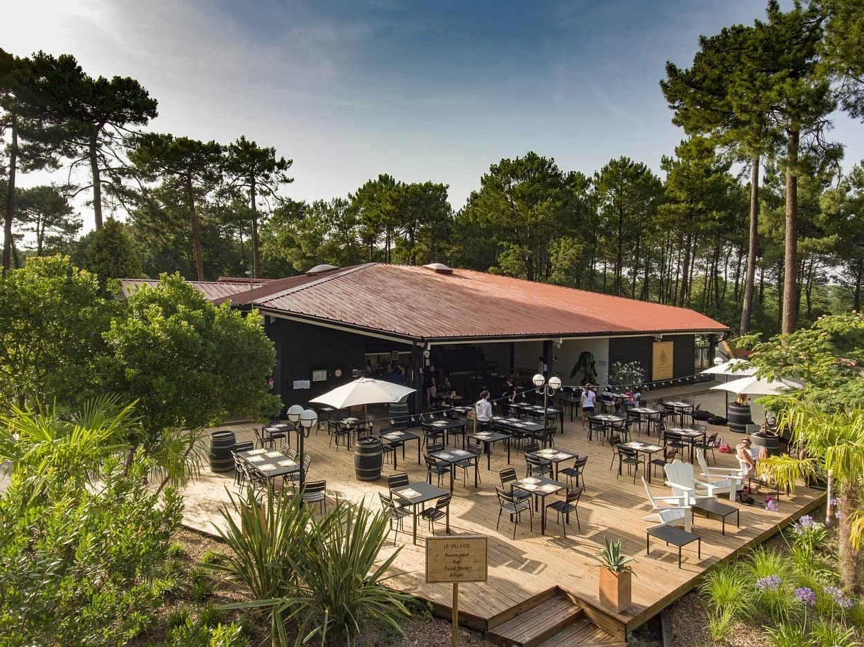 Terrasse du restaurant du Slow Village Biscarrosse Lac. La salle à manger en plein air est construite en bois et entourée d’une forêt dense de pins, idéale pour se reposer.