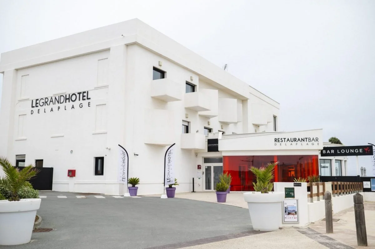 Façade extérieure du Grand Hôtel de la Plage à Biscarrosse. L’hôtel a un design blanc et moderne avec une entrée avec accent rouge, reflétant son style contemporain.