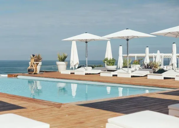 Piscine extérieure du Grand Hôtel de la Plage avec terrasse en bois, chaises longues blanches et parasols. L’espace offre une vue sur l’océan, idéal pour la détente.