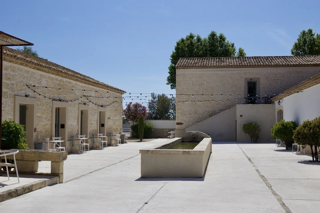 Cour principale du Domaine Le Sauvage en Camargue. Un espace extérieur d’architecture provençale en pierre avec une fontaine centrale et des lumières de chaîne pour les événements nocturnes.