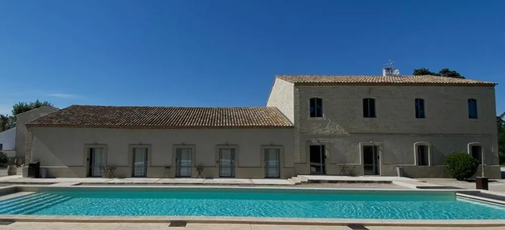 Piscine extérieure du Domaine Le Sauvage en Camargue, avec l’architecture de pierre du plus provençal reflétée dans l’eau sous un ciel bleu.