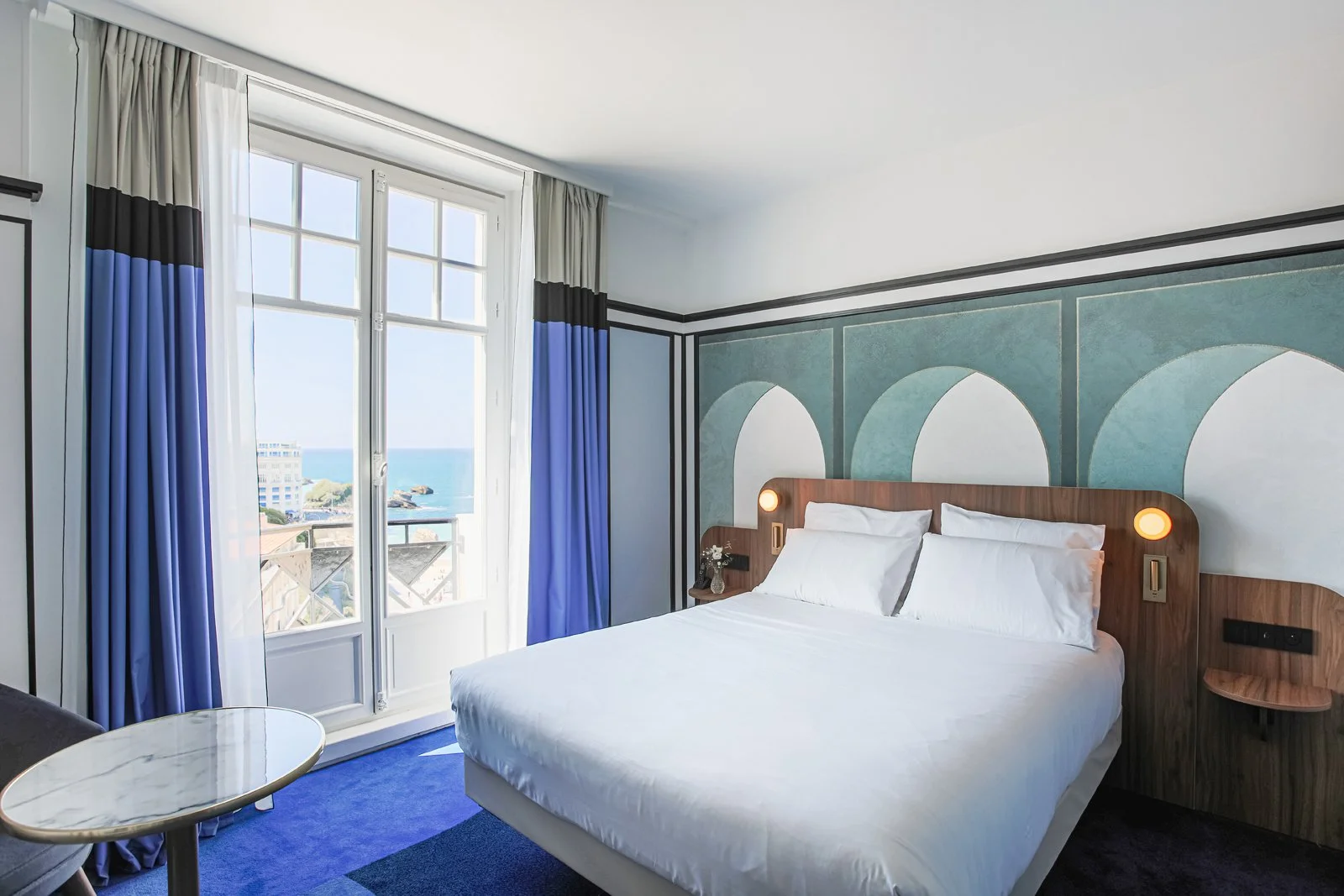 Chambre d’hôtel à l’Hôtel Mercure Plaza avec un design moderne et minimaliste, un grand lit et une grande fenêtre avec vue panoramique sur la mer.