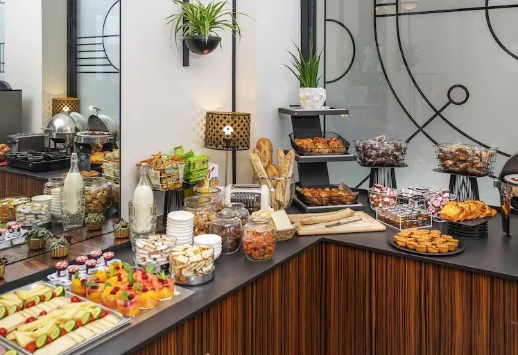 Petit-déjeuner buffet de l’hôtel Mercure Plaza avec une grande variété de fruits frais, yaourts et pâtisseries, présenté dans un bar moderne.