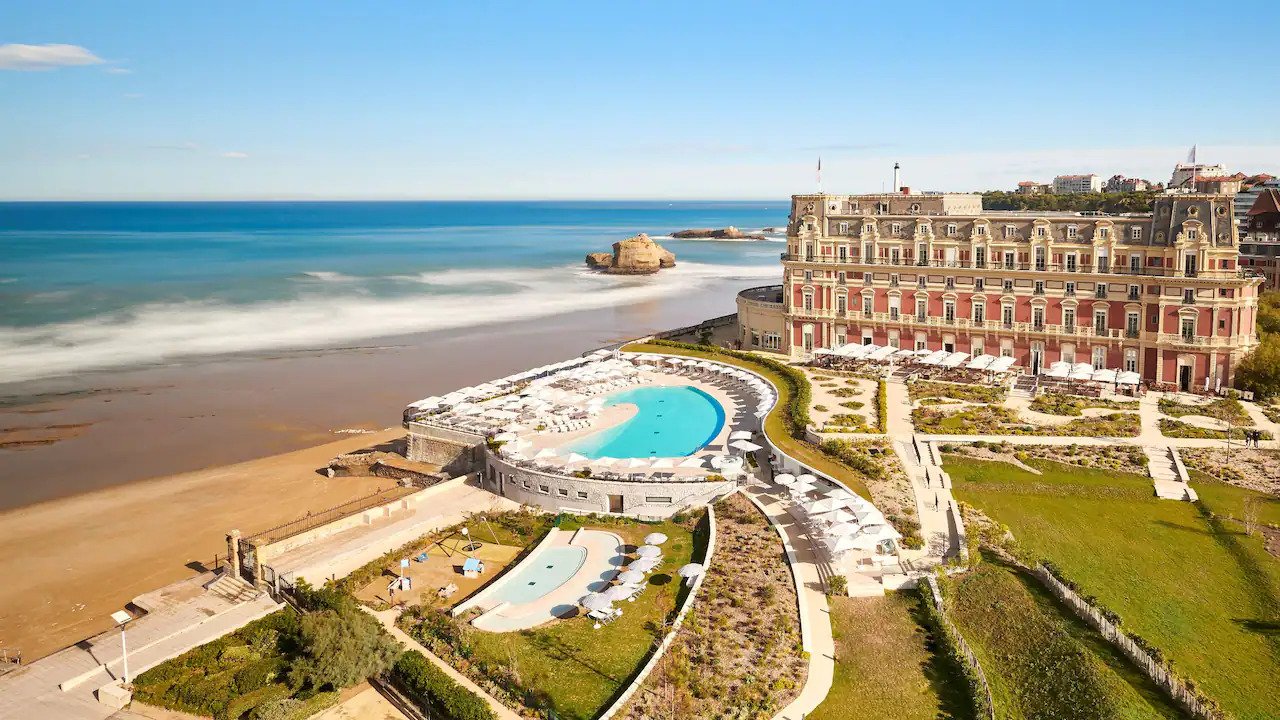 Vue aérienne de l’emblématique Hôtel du Palais à Biarritz, un palais de luxe face à la mer. Le complexe dispose d’une grande piscine incurvée, de vastes jardins et d’un accès direct à la plage.