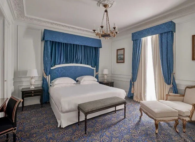 Chambre de luxe à l’Hôtel du Palais avec un lit à baldaquin et des rideaux bleus, décorée dans un style classique et élégant, en accord avec l’histoire du palais.