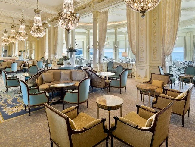 Salon d’hôtel à l’Hôtel du Palais avec mobilier de luxe dans des tons dorés et bleus. L’espace, avec de grandes fenêtres, offre une atmosphère élégante et sophistiquée pour les invités.