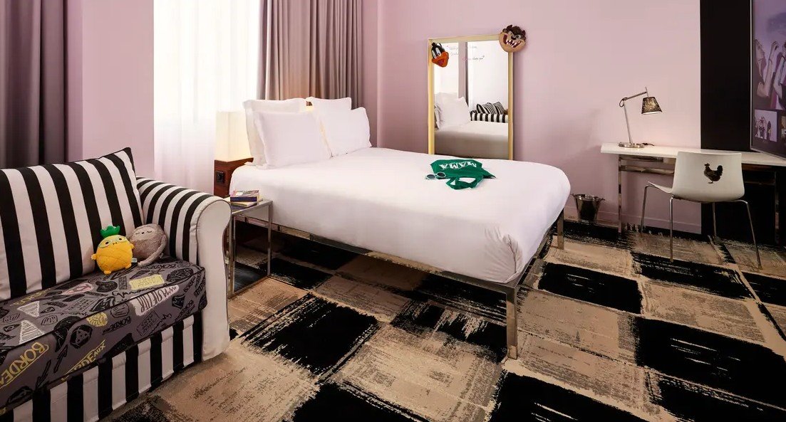 Chambre d’hôtel au Mama Shelter Bordeaux avec un design graphique et moderne, literie à rayures et miroir décoratif, dans un style fonctionnel et audacieux.