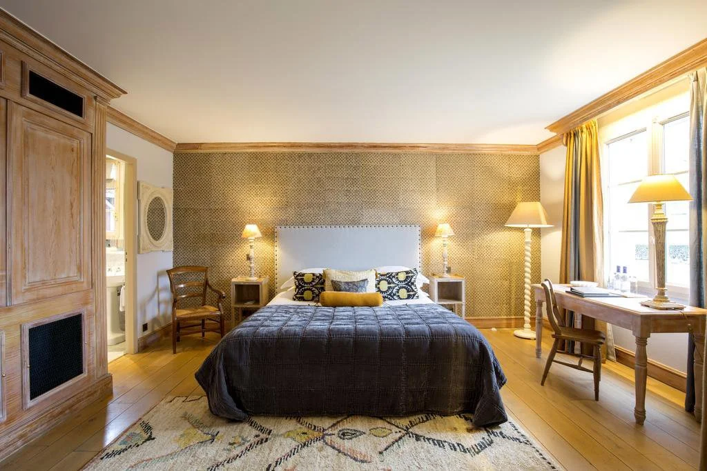 Chambre de luxe à l’Hôtel Les Sources de Caudalie, avec un grand lit, mobilier en bois classique et papier peint texturé, créant une atmosphère élégante et accueillante.